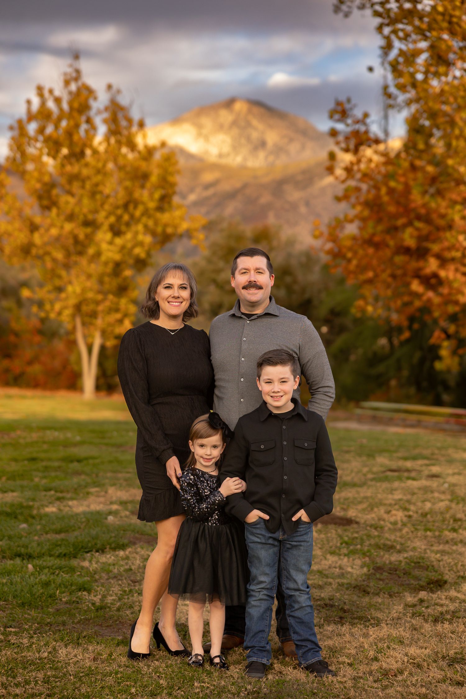 A family poses for a portrait with autumn trees and mountains in the background.