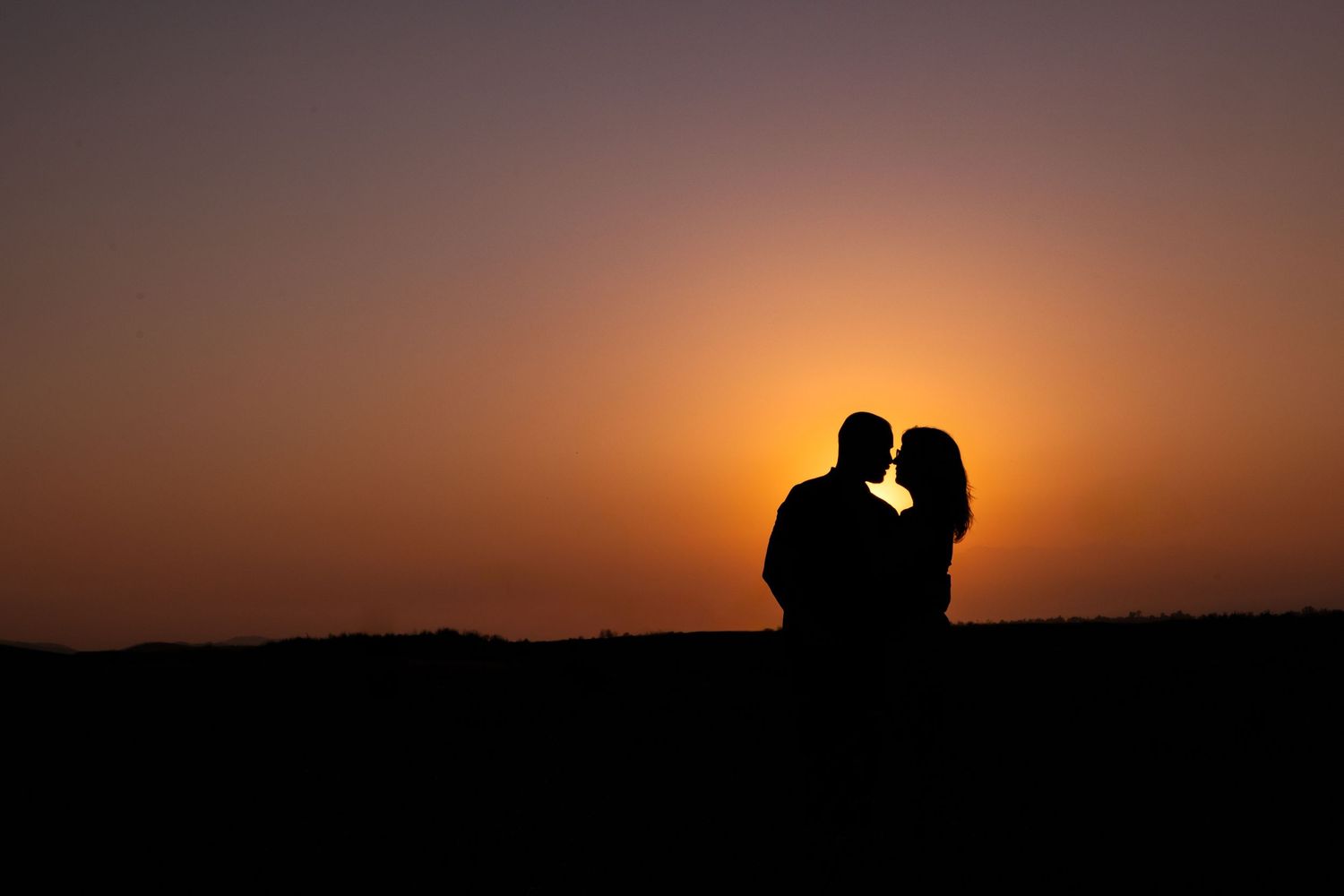 Silhouettes of two people against a dramatic orange sunset sky.