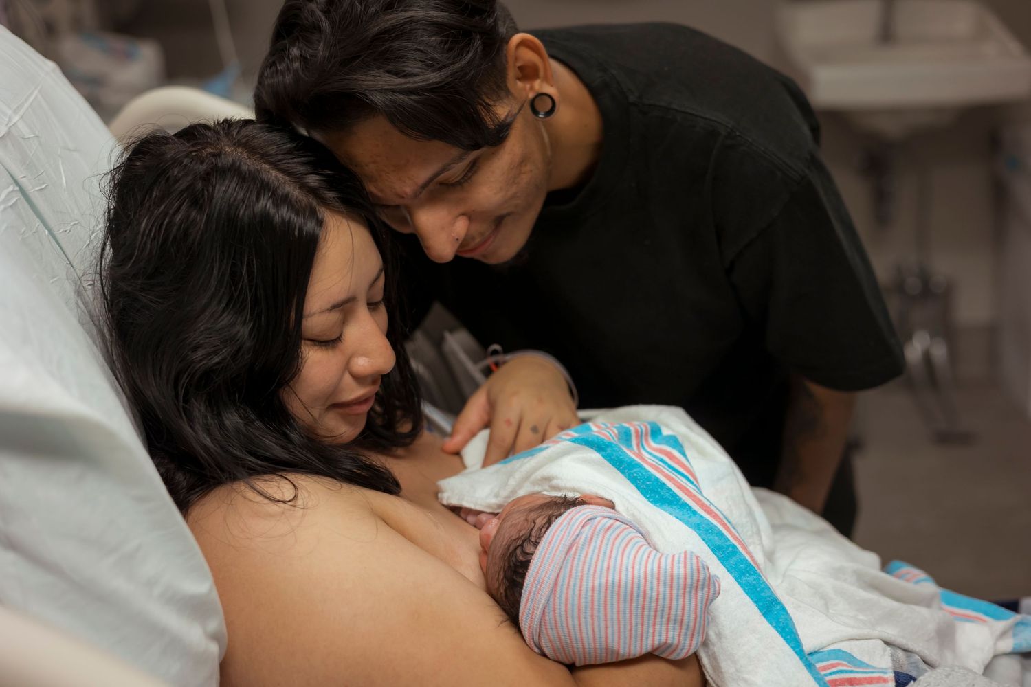 New parents share an intimate moment with their newborn baby in hospital room.