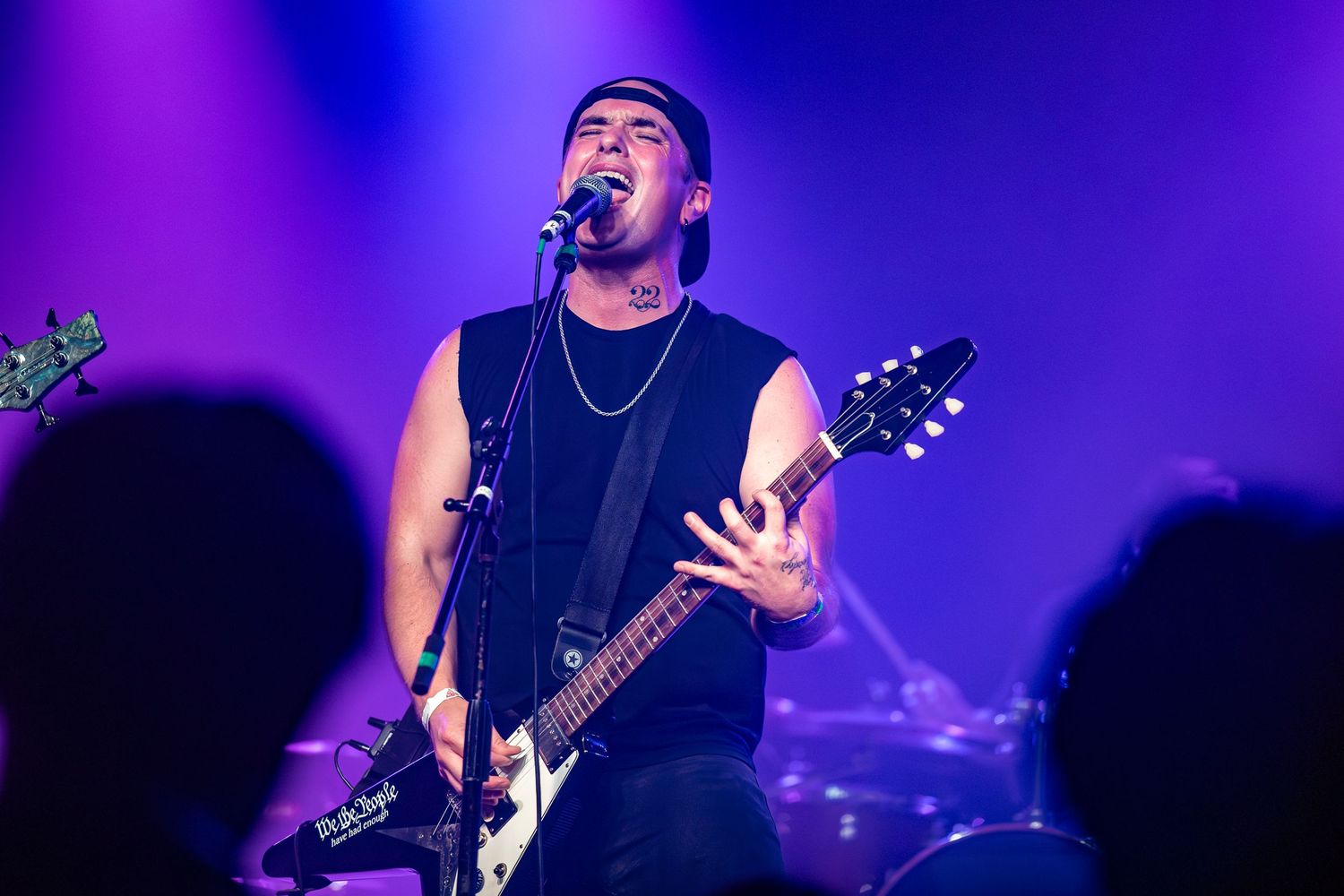Concert performer in a black tank top sings and plays guitar under purple stage lighting during energetic live show in Pomona.