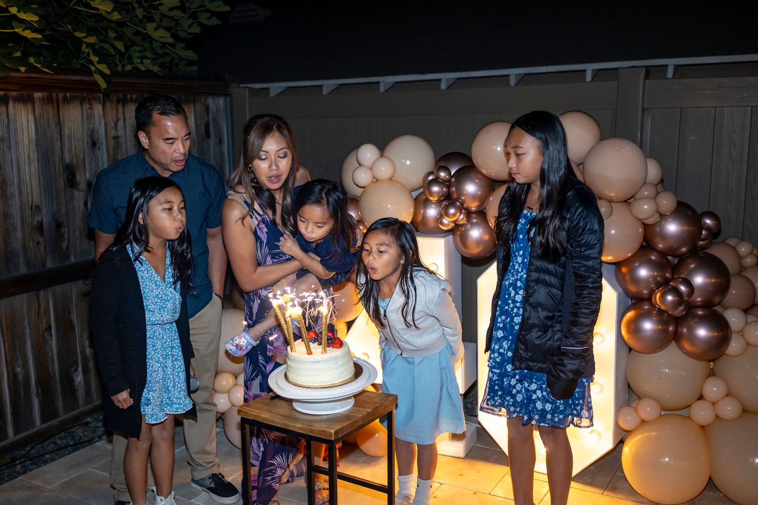 Family gathering around birthday cake with balloon decorations in backyard setting in Anaheim.