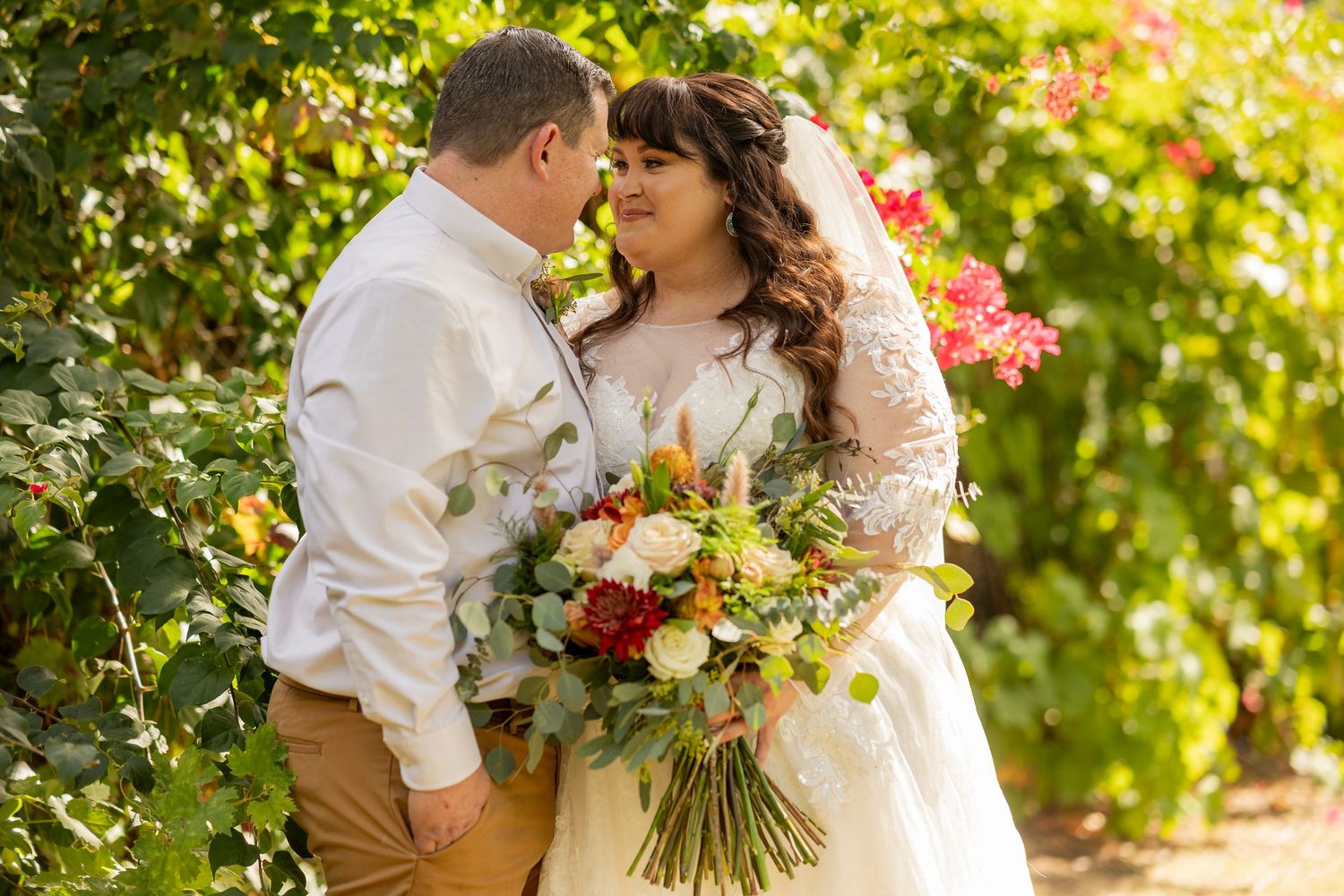 Romantic wedding portrait with floral bouquet against vibrant garden backdrop.