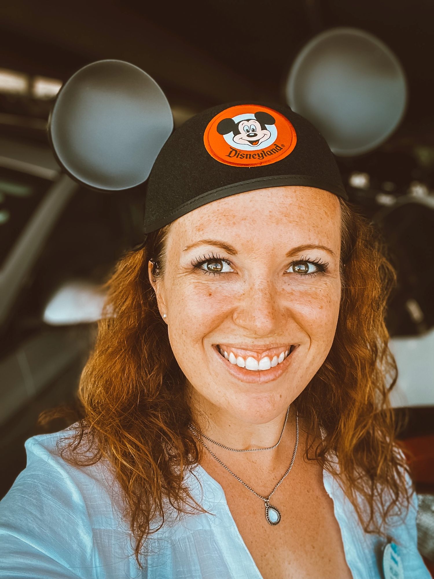 Person wearing orange Mickey Mouse cap and white shirt smiling outdoors.