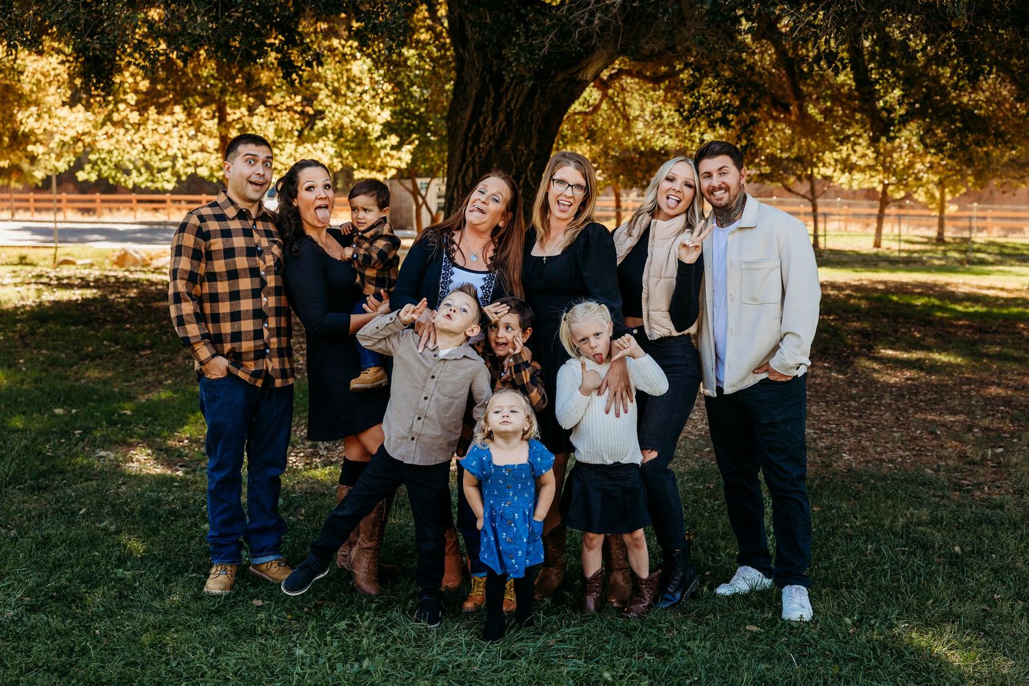 Family group portrait outdoors in casual attire during autumn with natural lighting and fall foliage.