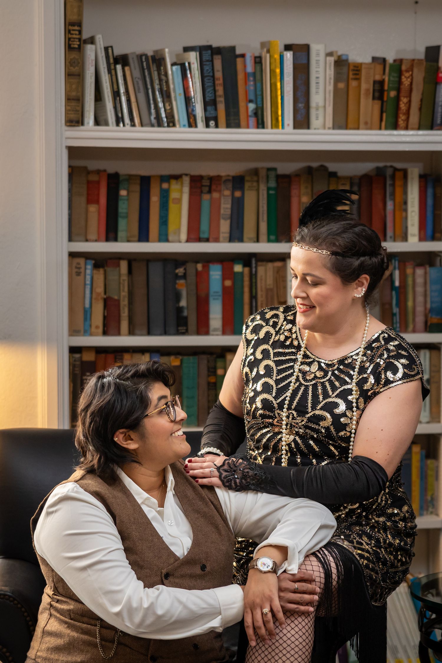 A couple poses playfully for photos in a library with bookshelves in the background.