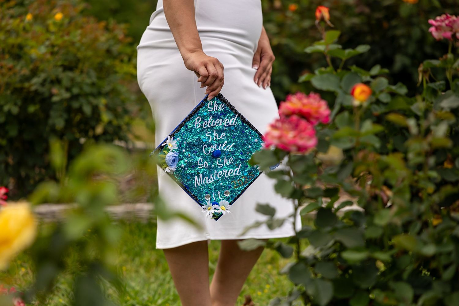 Decorated graduation cap with teal design against floral garden background in Riverside.