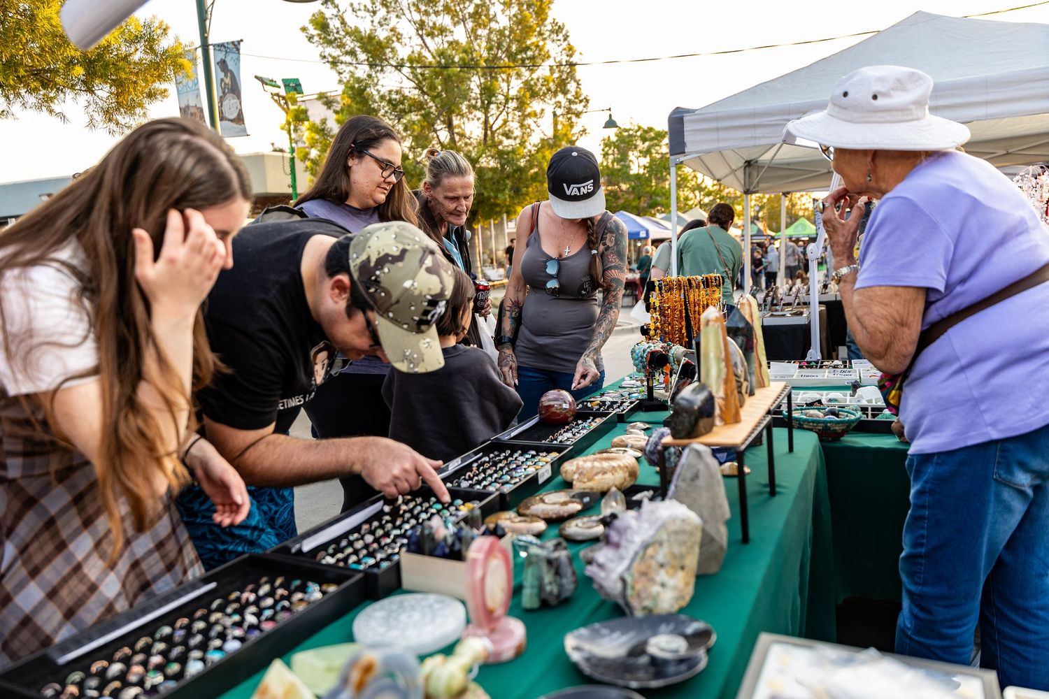 Group of people examining merchandise at an outdoor market vendor stall.