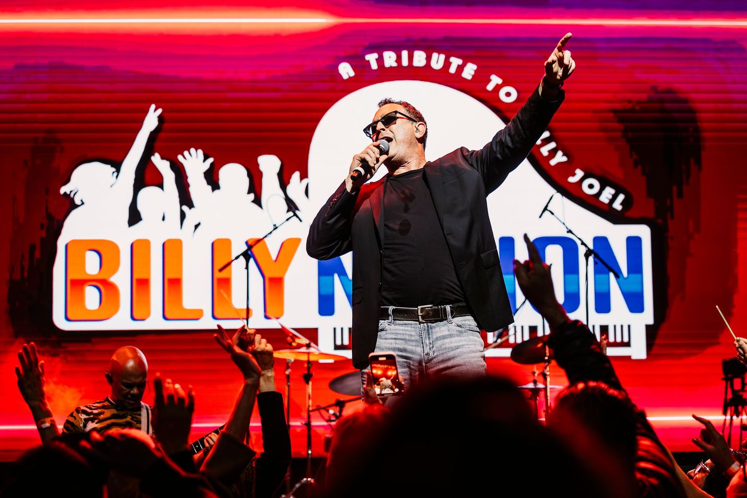 Energetic concert performance with red lighting and Billy Nation branding displayed on stage screen in Garden Grove.