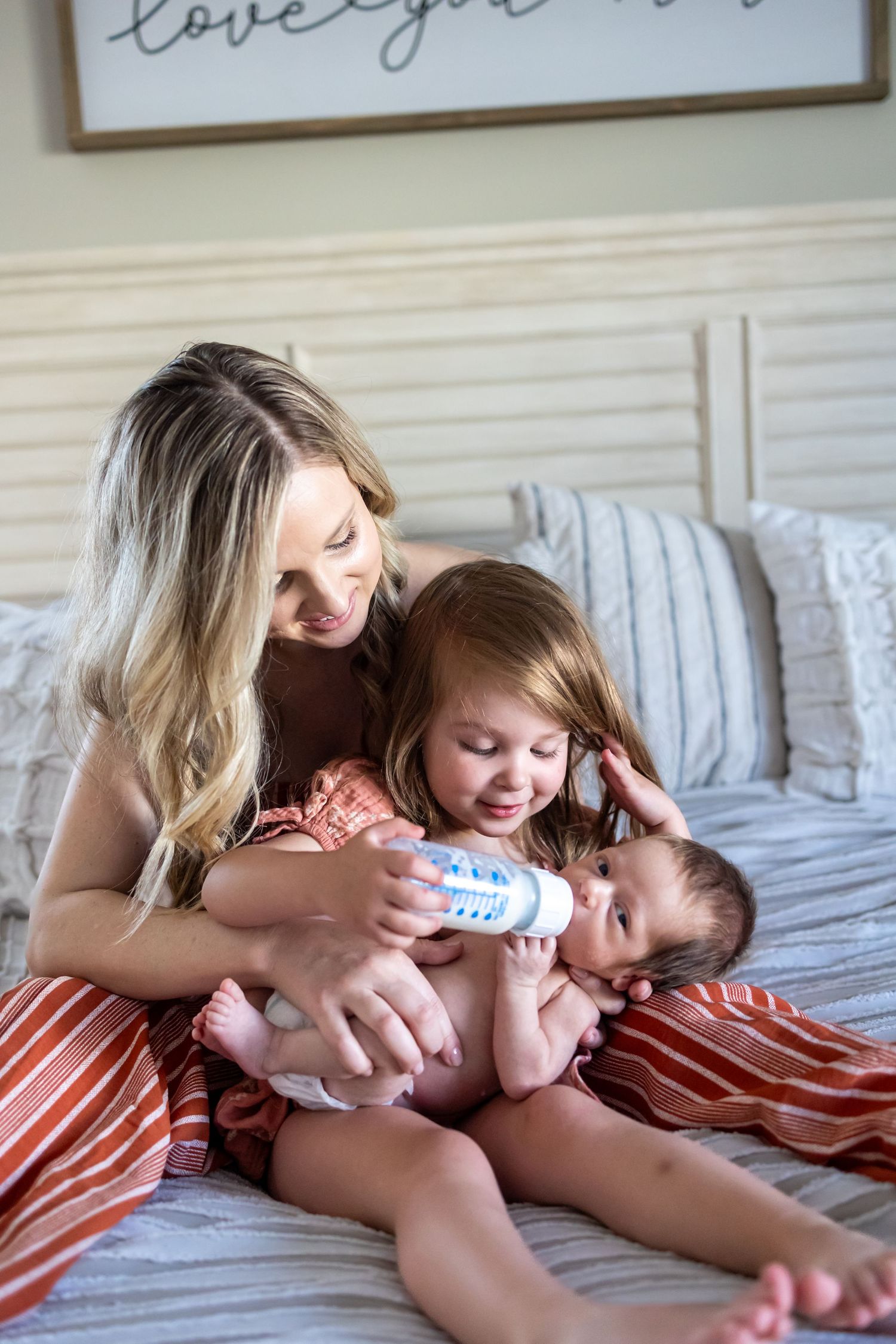 Sweet moment of bottle feeding baby with big sister and little brother at home in Beaumont
