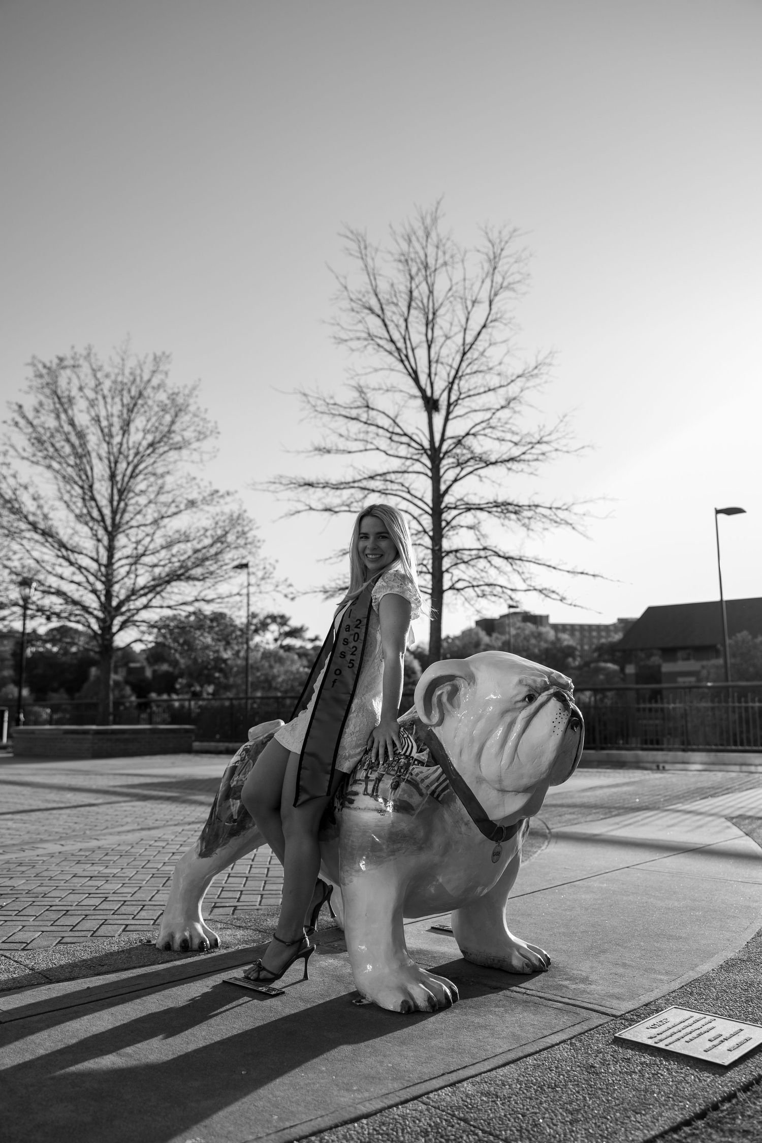 Graduate poses on decorative campus bulldog statue in black and white photo.