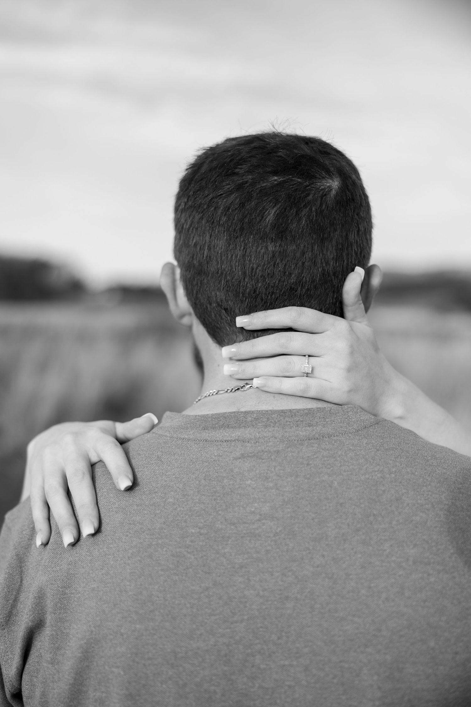A close-up view of hands embracing on a person's shoulder wearing a gray shirt.