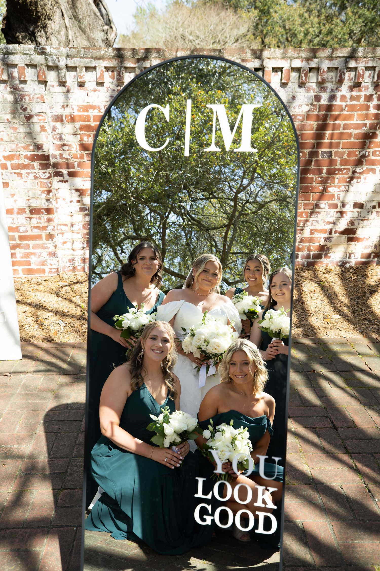 Wedding party poses against rustic brick wall in teal and white outfits with floral bouquets.