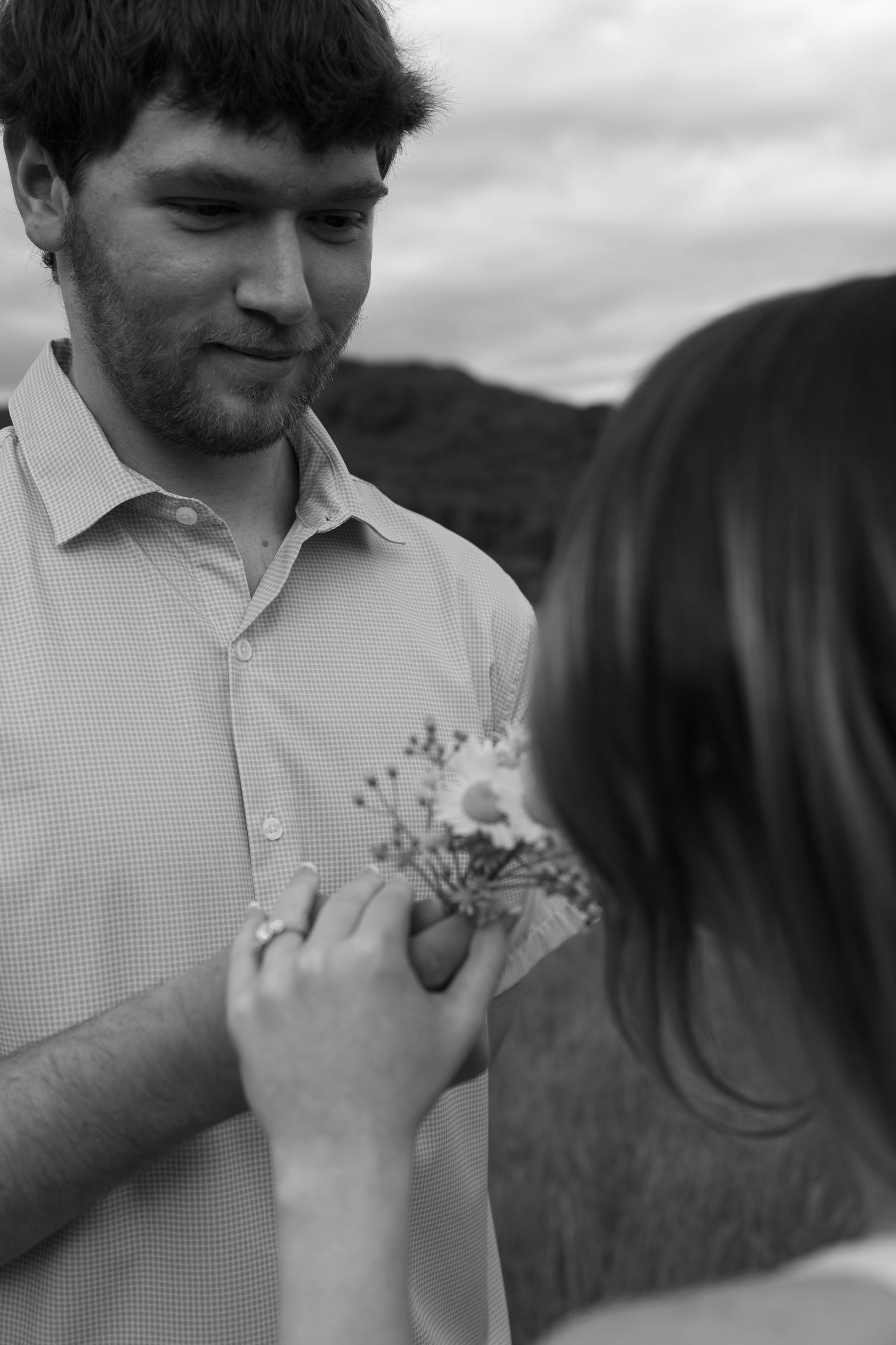 A tender black and white moment showing hands holding small flowers outdoors.