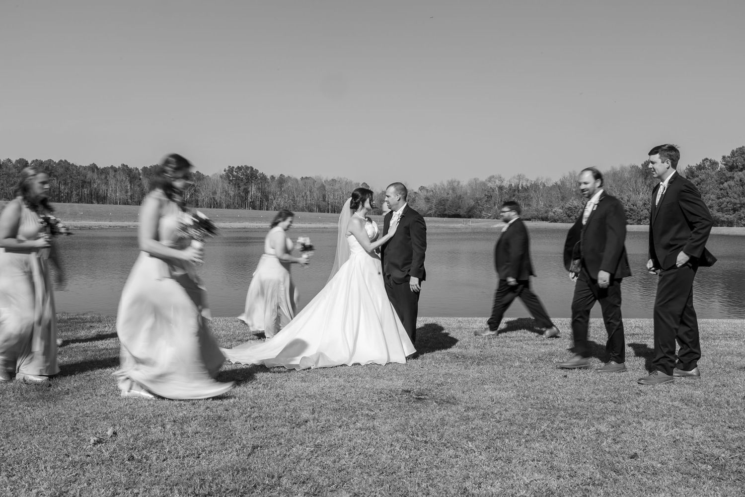 Wedding party poses creatively with bridesmaids and groomsmen running across a grassy field.