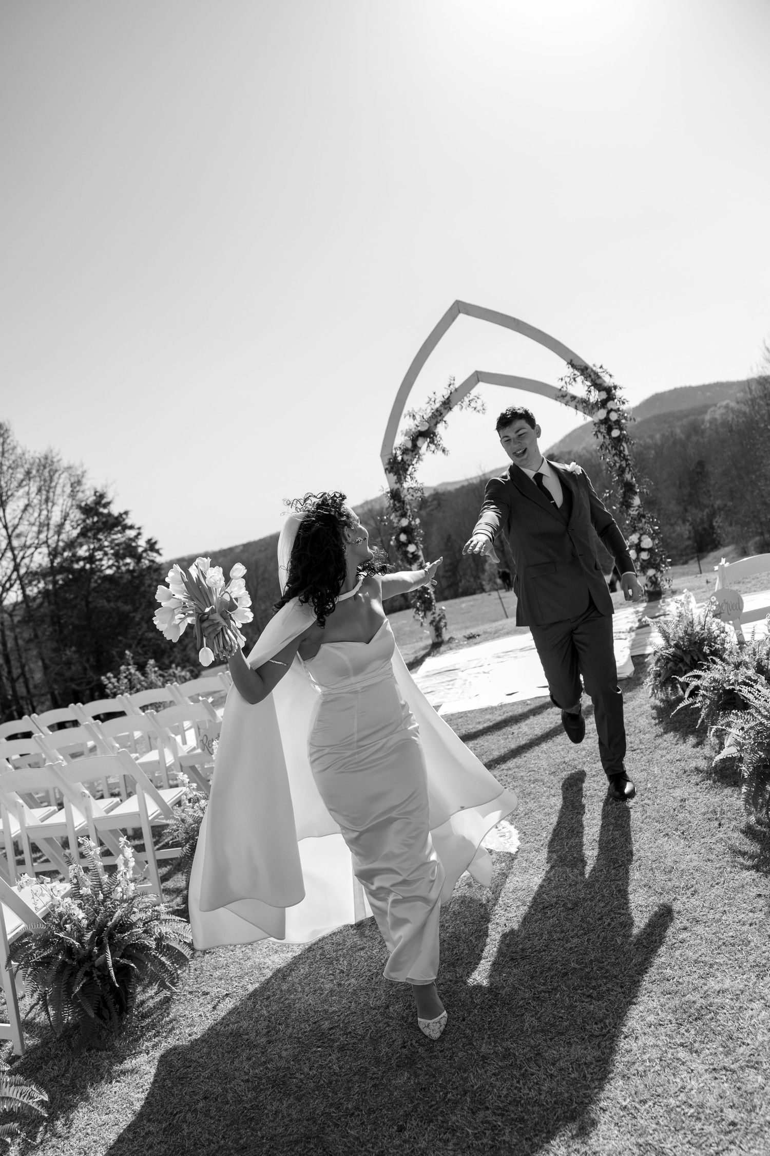 Black and white photo of newlyweds running joyfully after outdoor ceremony.