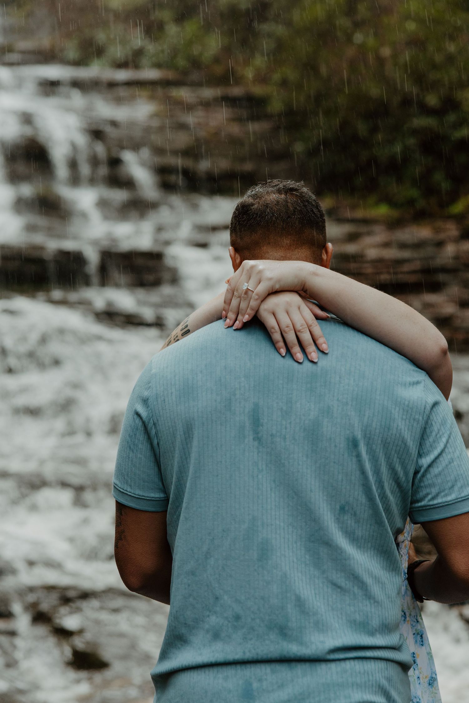 A romantic embrace near a waterfall with arms wrapped around turquoise shirt.