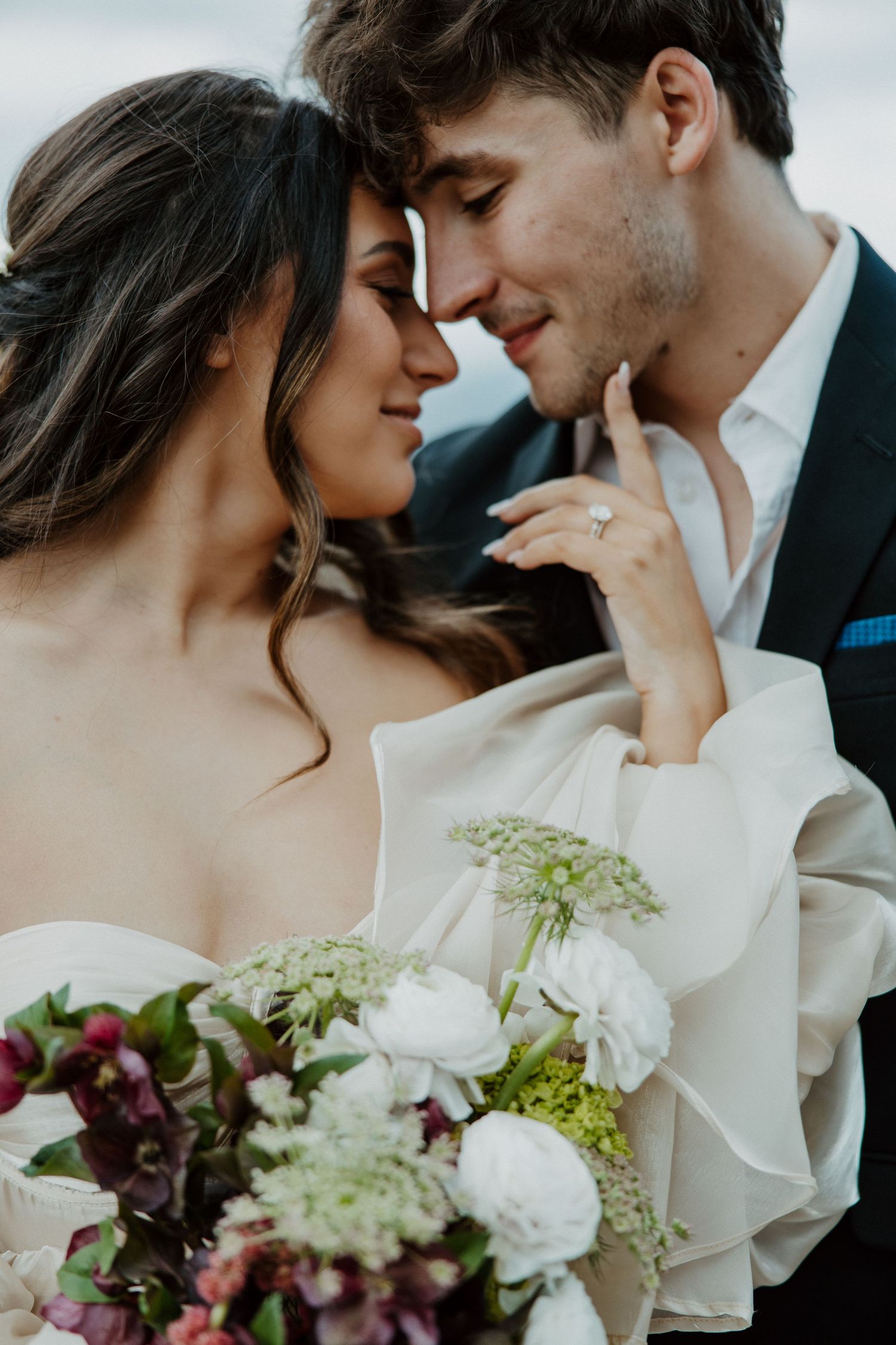 Romantic wedding couple embracing with a lush bouquet of mixed flowers between them.