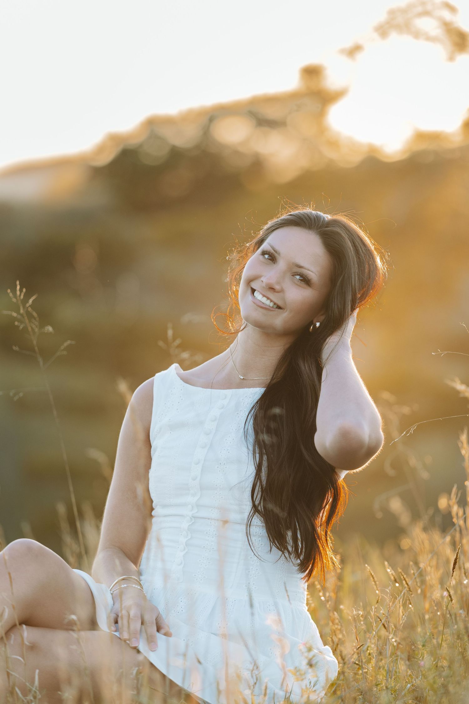 Woman in white dress sitting in sunlit meadow during golden hour.