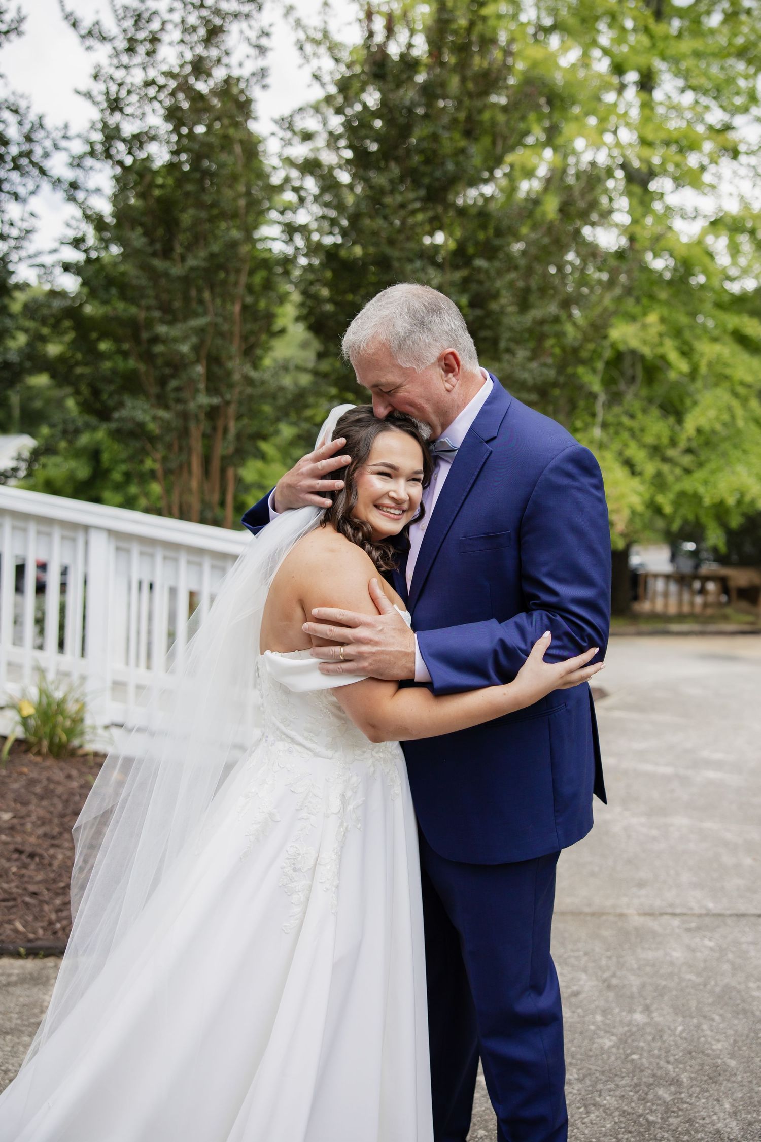 A tender moment between a bride in white and a groom in navy blue sharing an embrace outdoors.