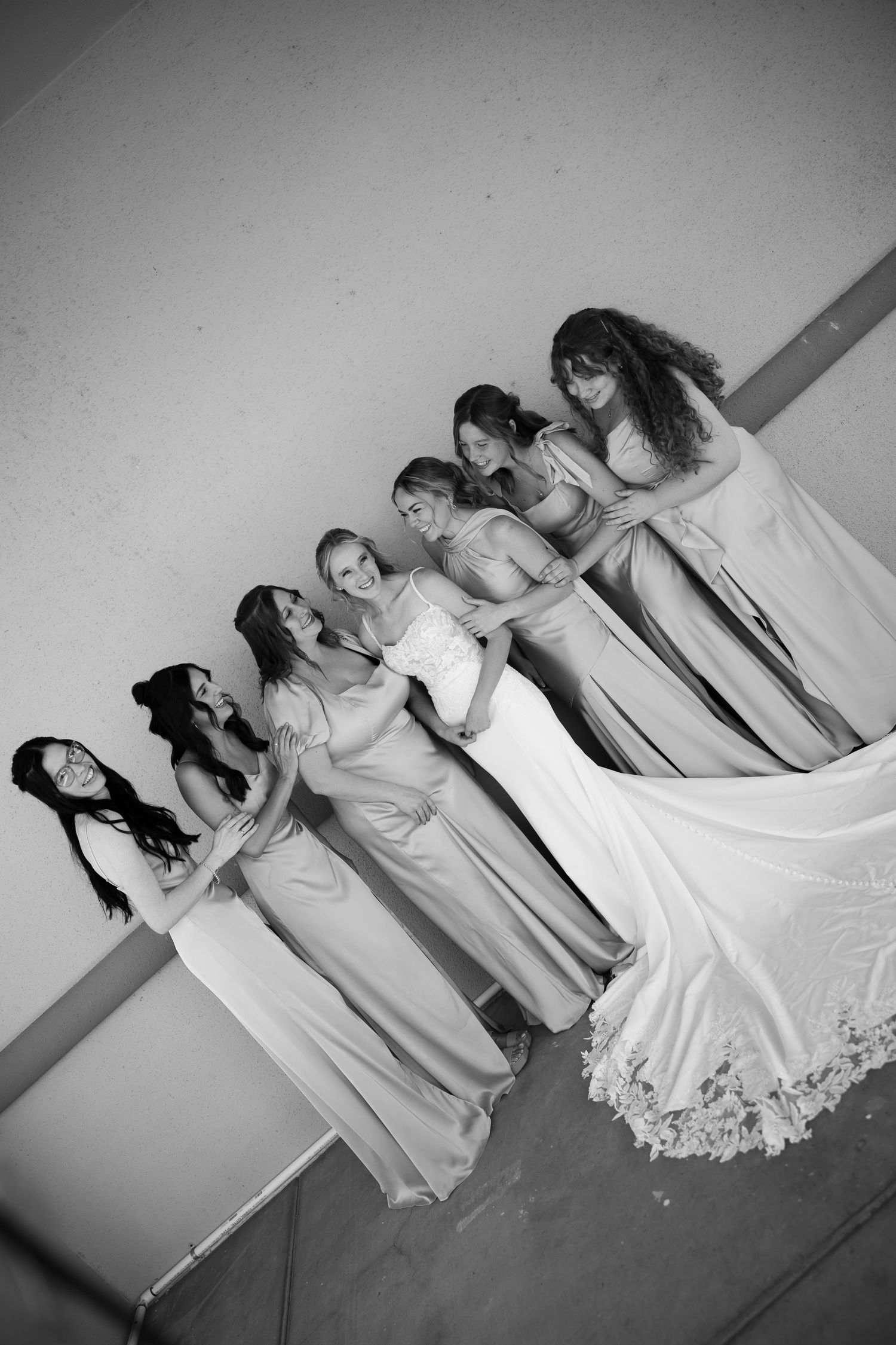 Black and white photo of a bride in a white gown with six bridesmaids in elegant dresses, posing together at a wedding.
