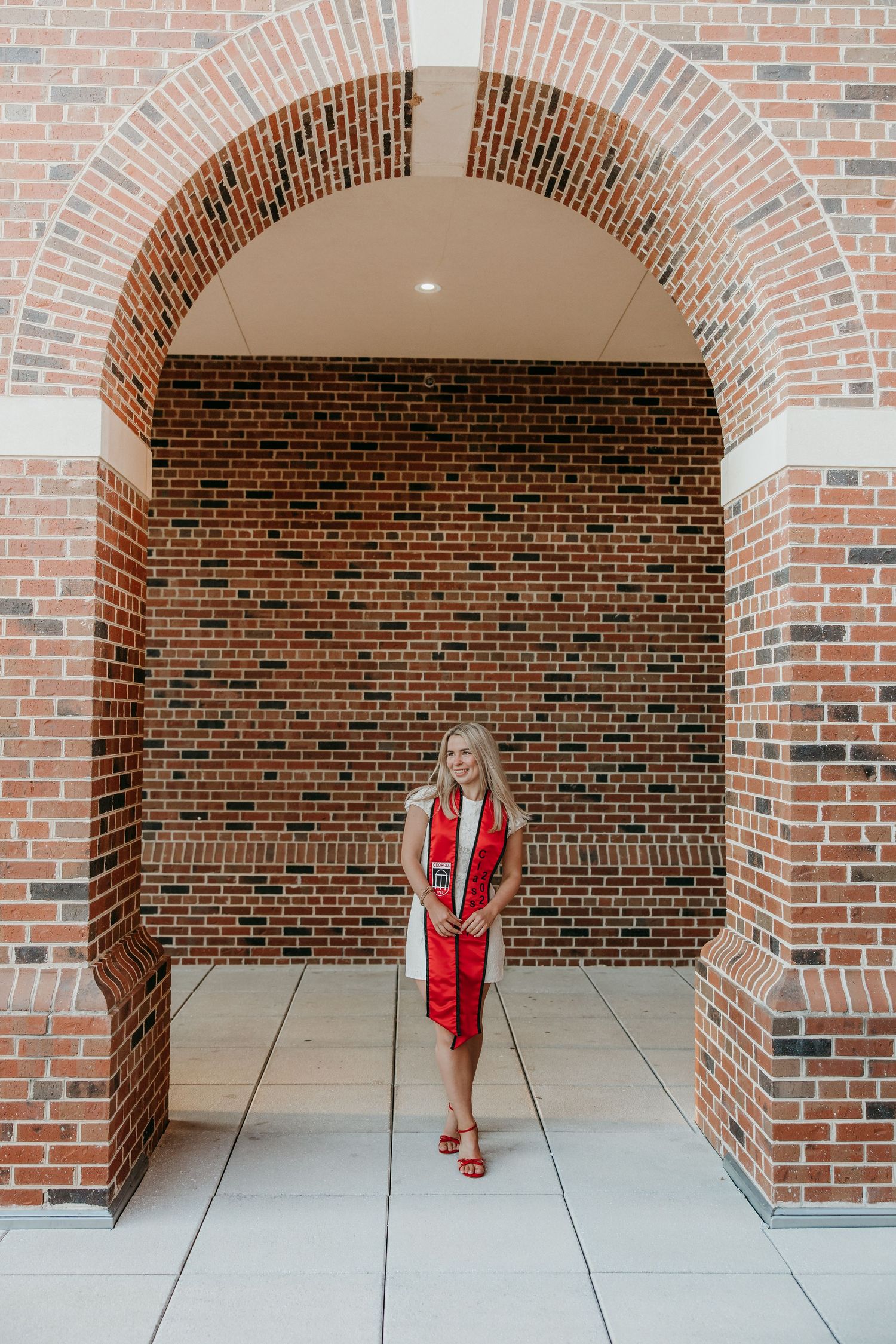 Graduate stands under brick archway wearing graduation regalia.