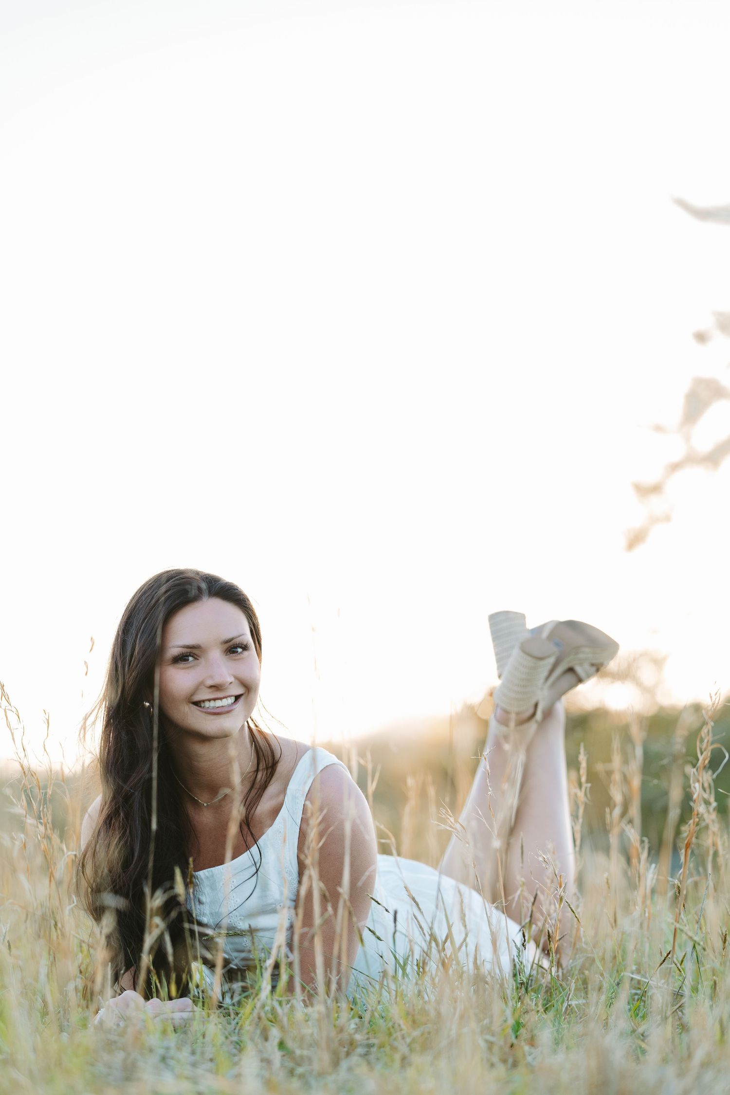 Woman in white dress lying in tall grass during sunset.