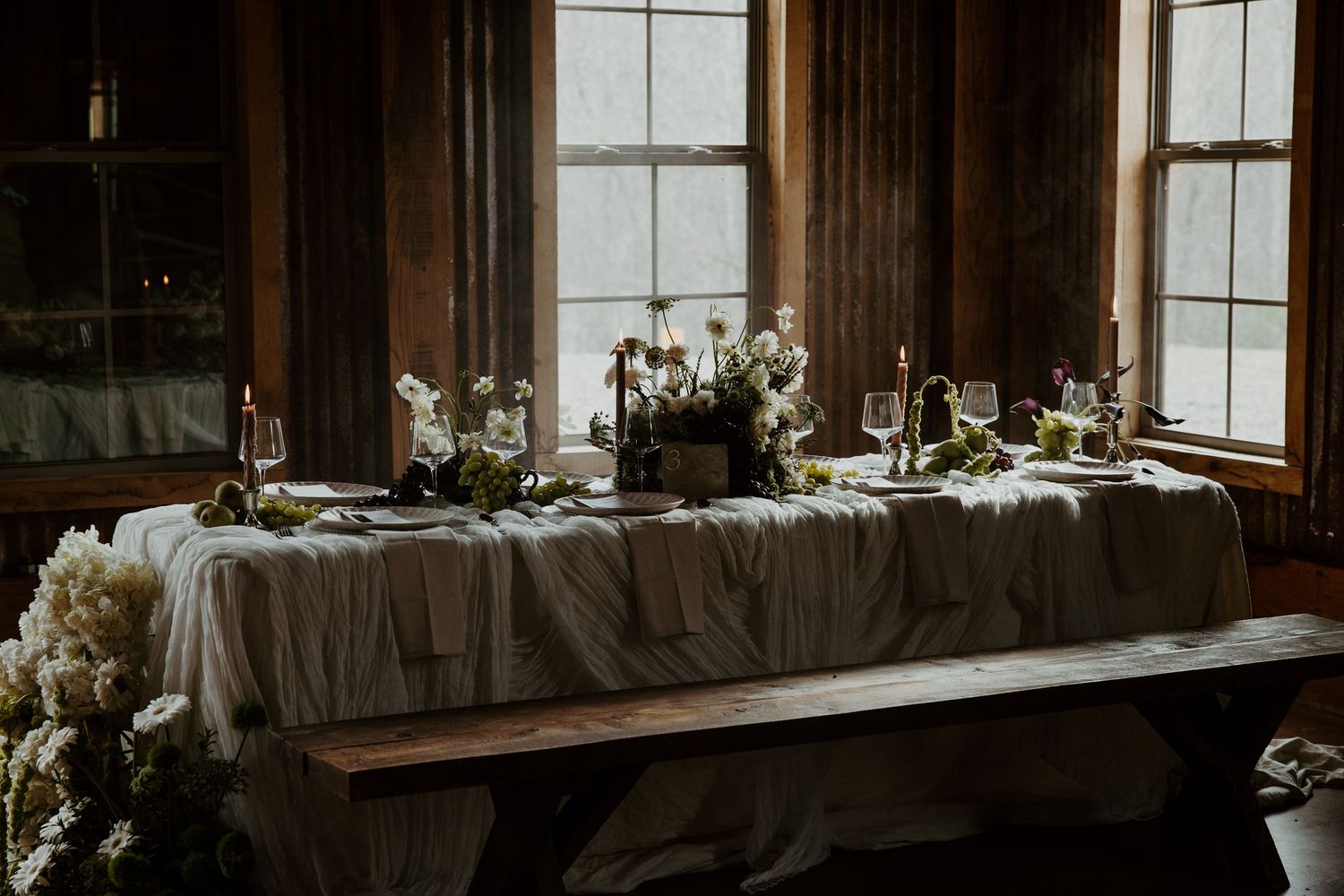 Elegant rustic wedding reception table with gray linens and floral centerpieces in a wooden room.
