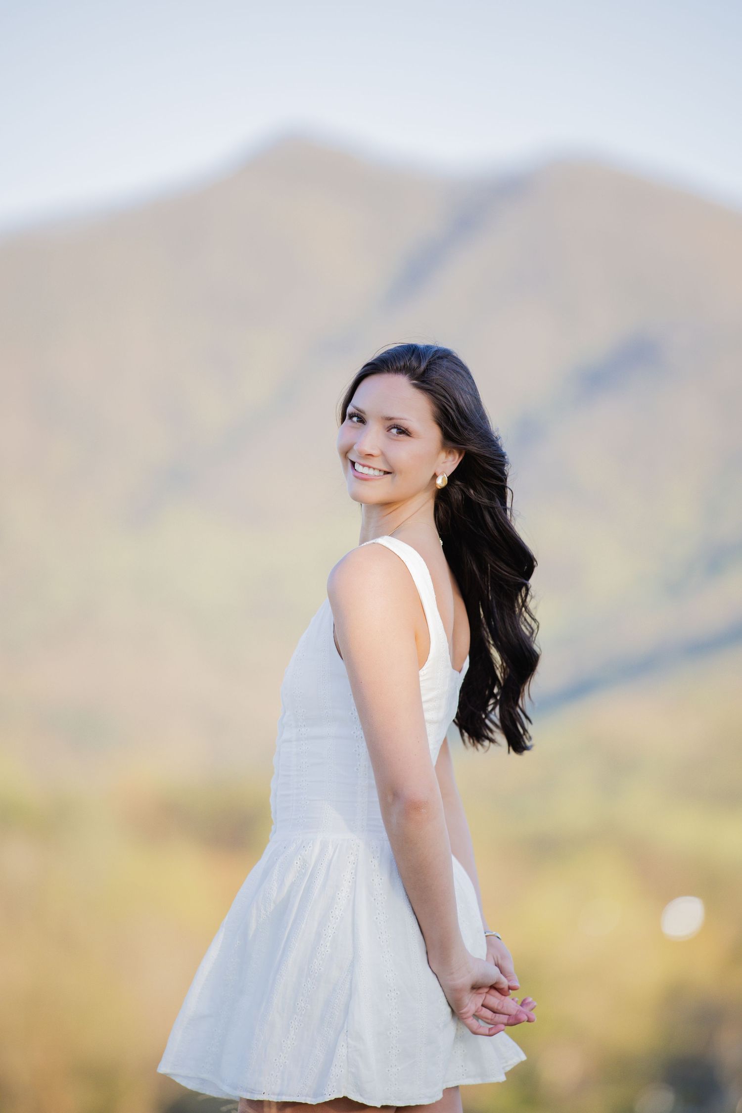 Person in white dress twirls against desert mountain landscape during sunset.