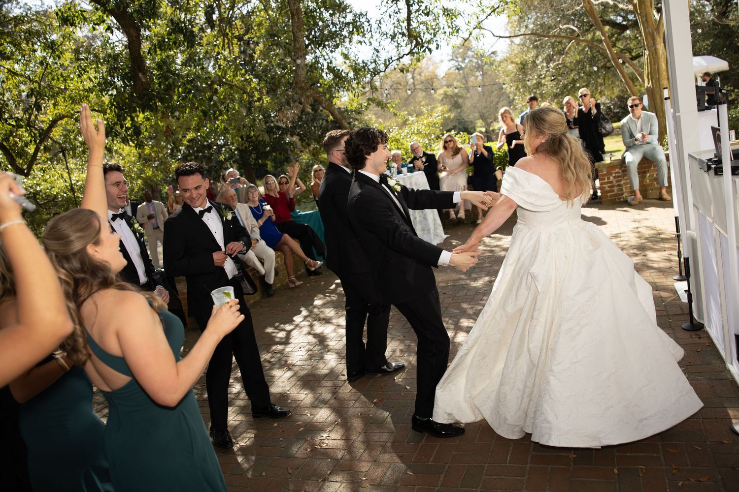 A couple shares their first dance at an outdoor wedding ceremony surrounded by guests and natural greenery.