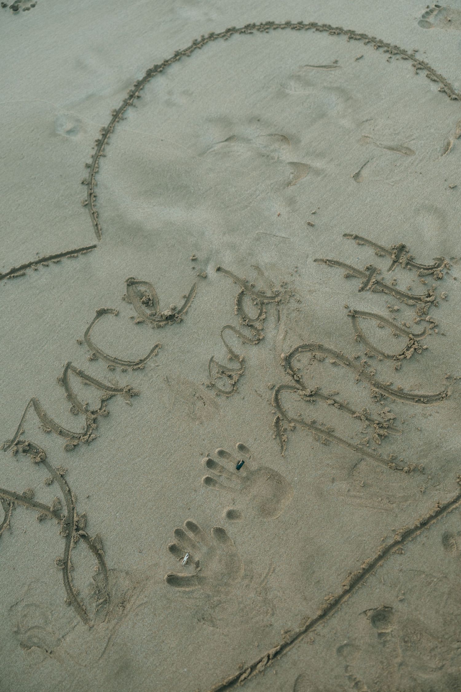 Writing and doodles drawn in wet sand at the beach with chain-like patterns visible.