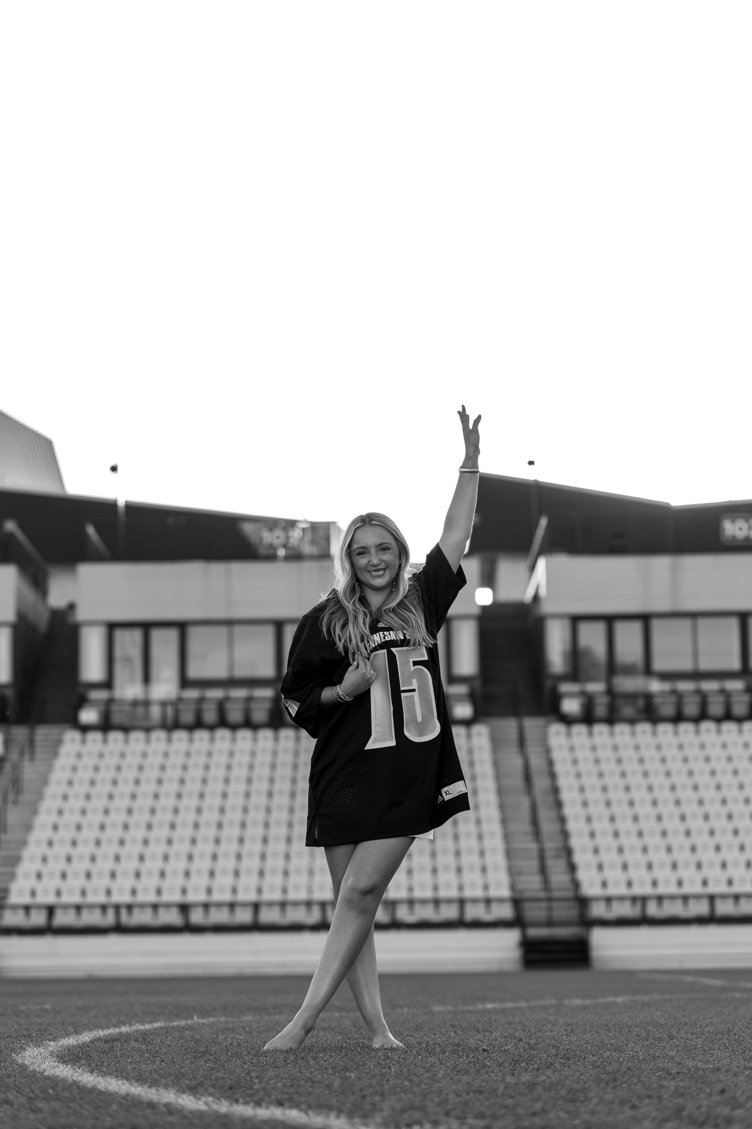 Black and white photo of graduate celebrating in stadium wearing sports jersey.