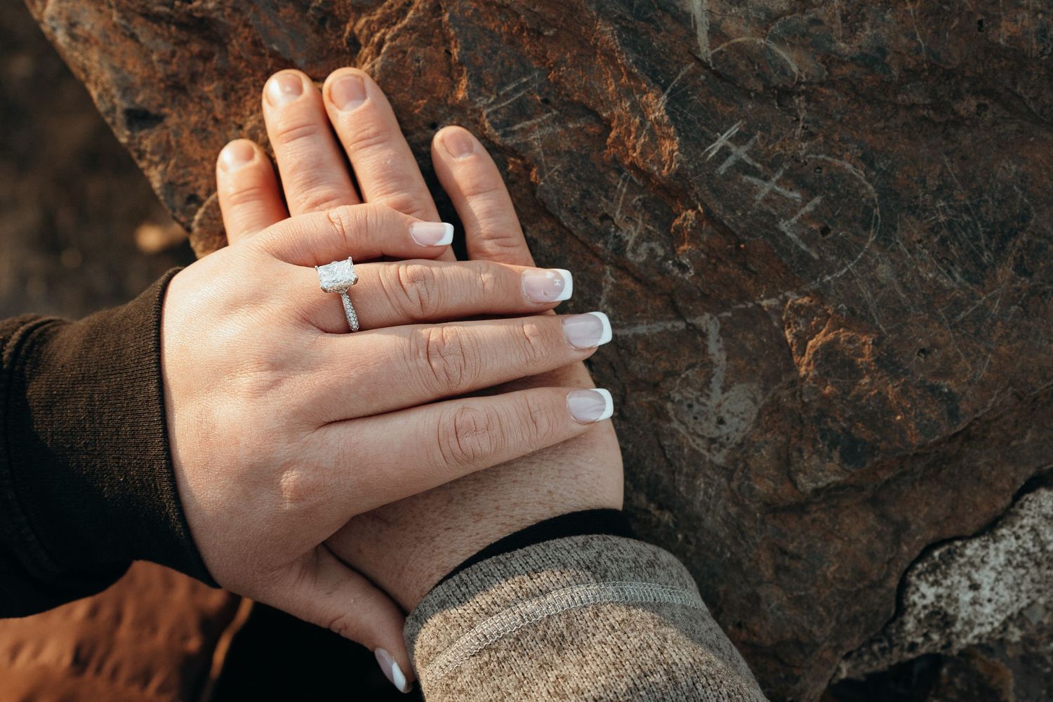 Hands tenderly touching against rocky background in warm light.