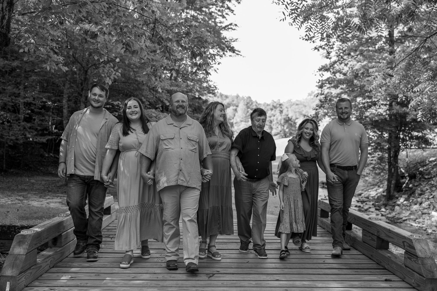 A group of people walking together on a wooden bridge in a park setting, captured in black and white.