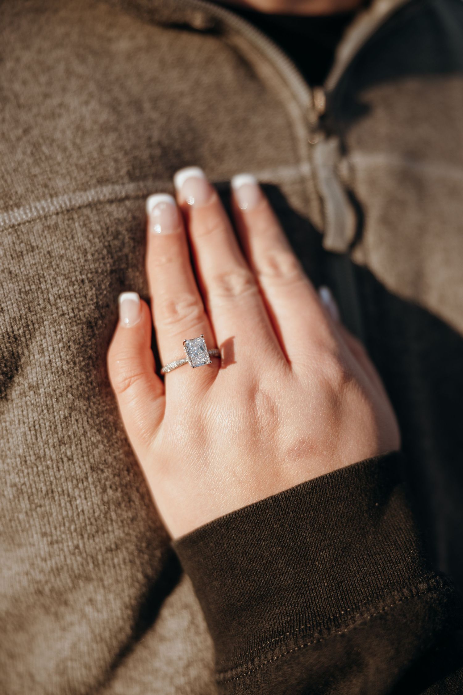 Close-up of an engagement ring on a hand against a brown sweater.