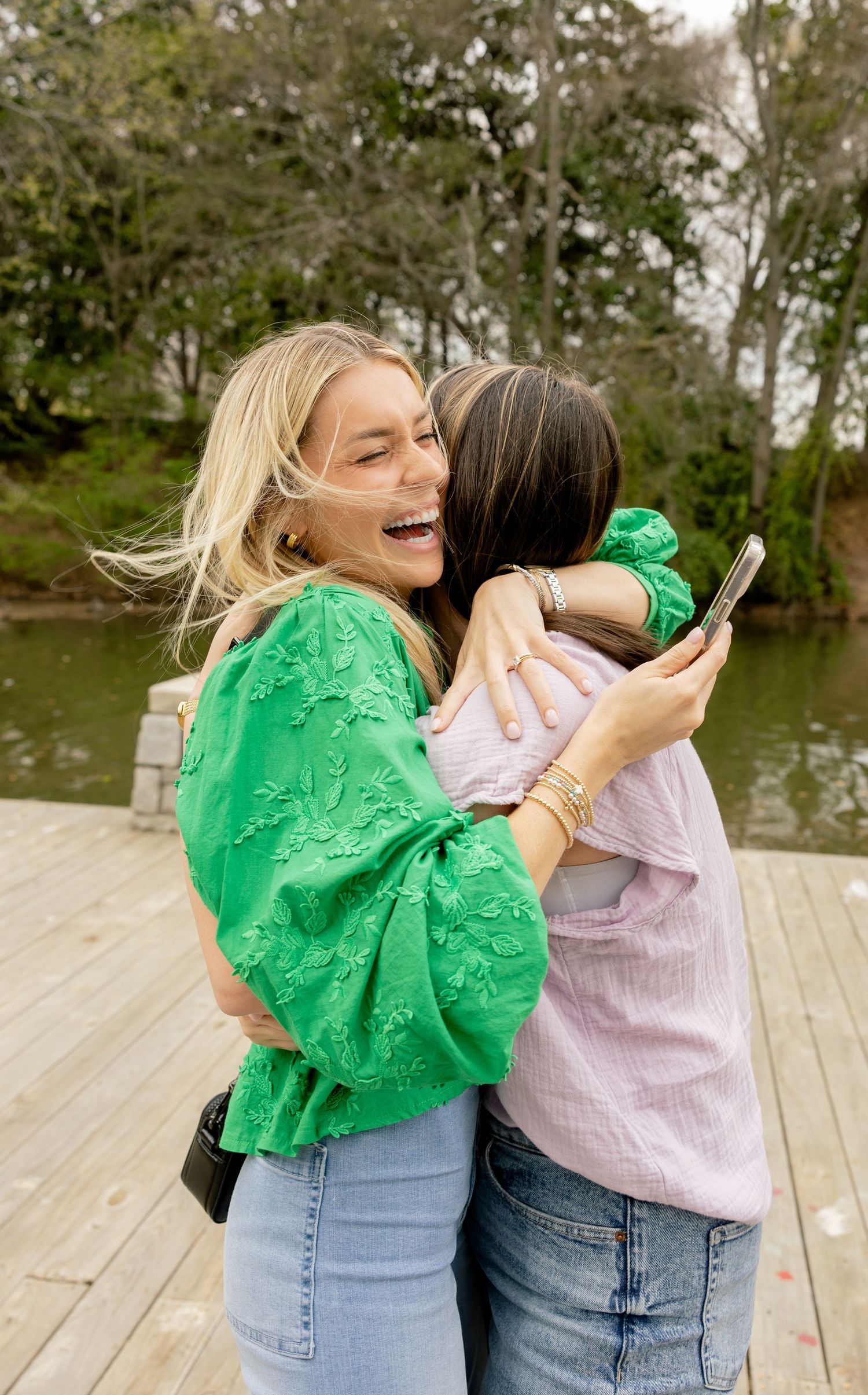 Two friends share an emotional embrace on a wooden dock by a lake.