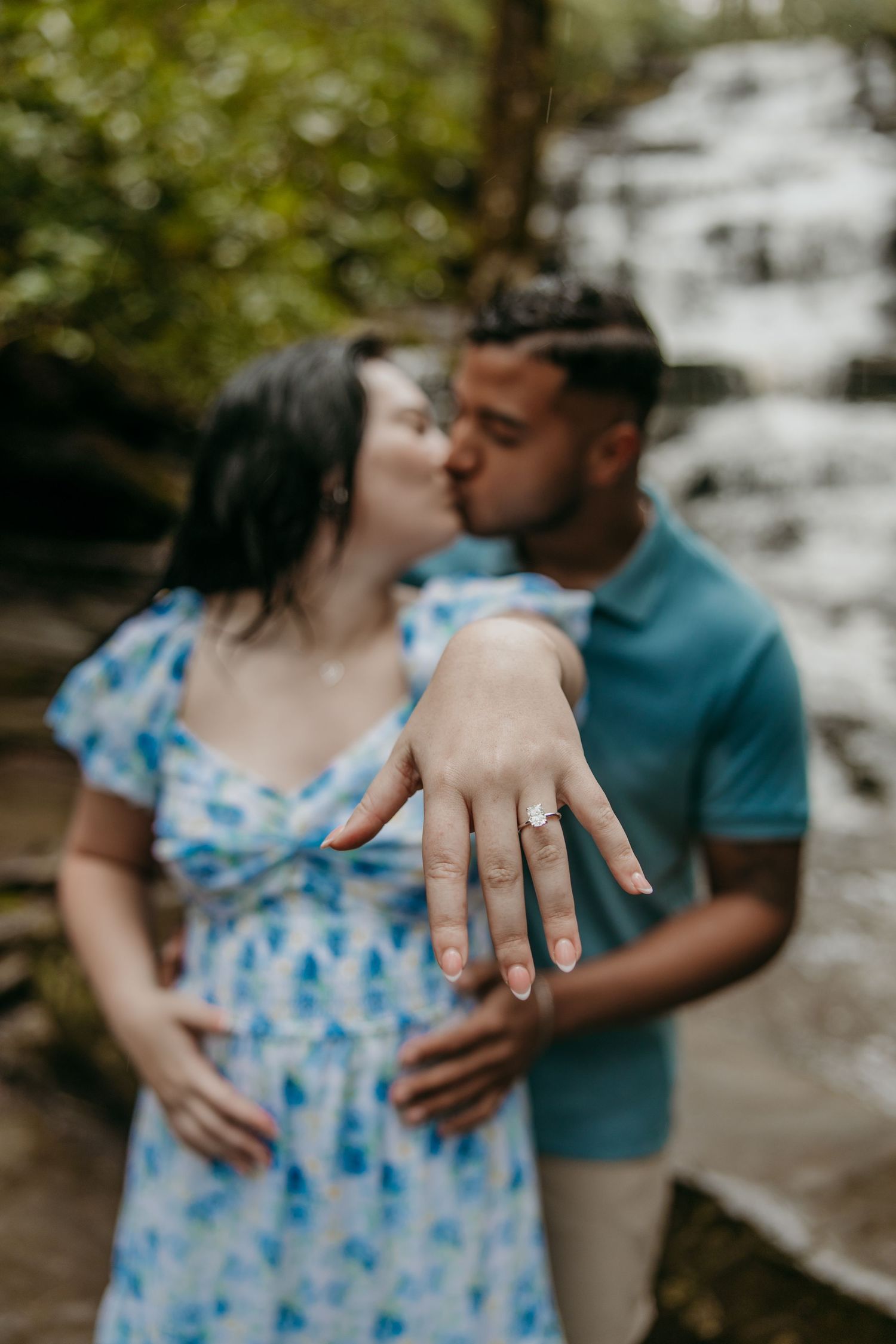 An intimate moment shared in front of a waterfall while displaying an engagement ring.