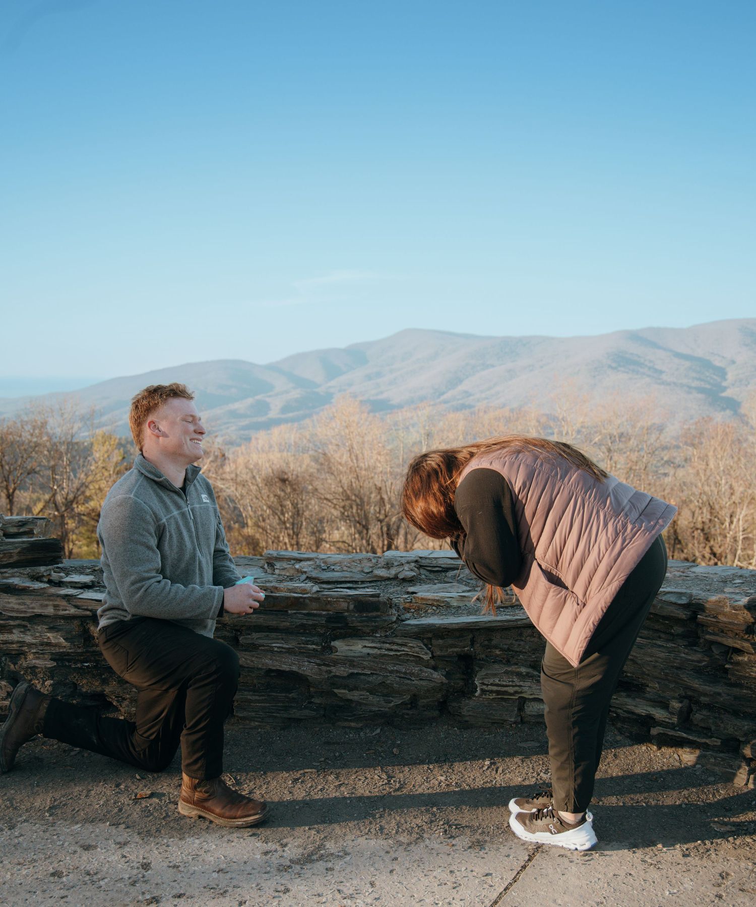 A couple engaging in a romantic surprise moment in a mountainous landscape.