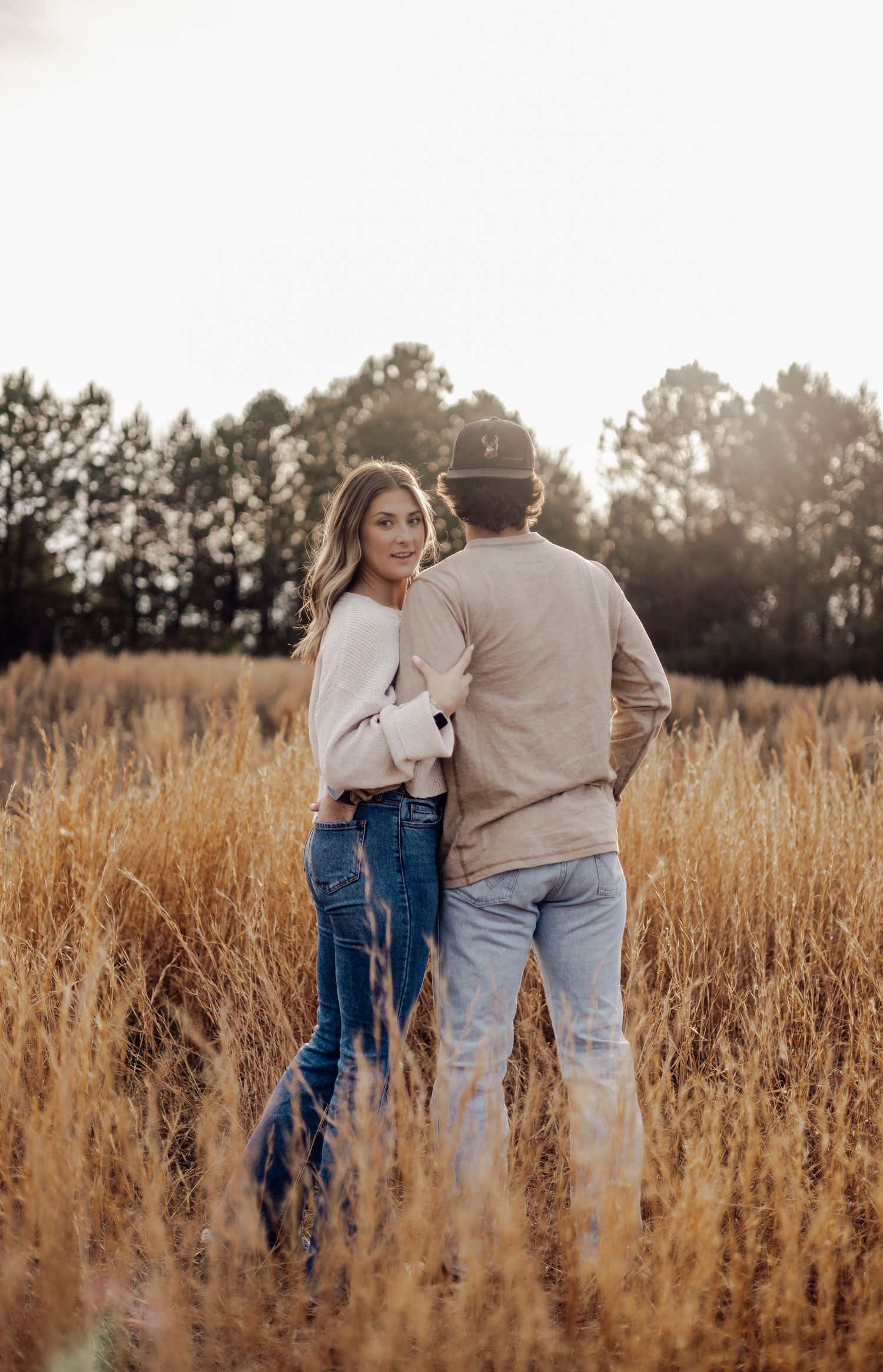 A couple walking through a golden field during sunset.