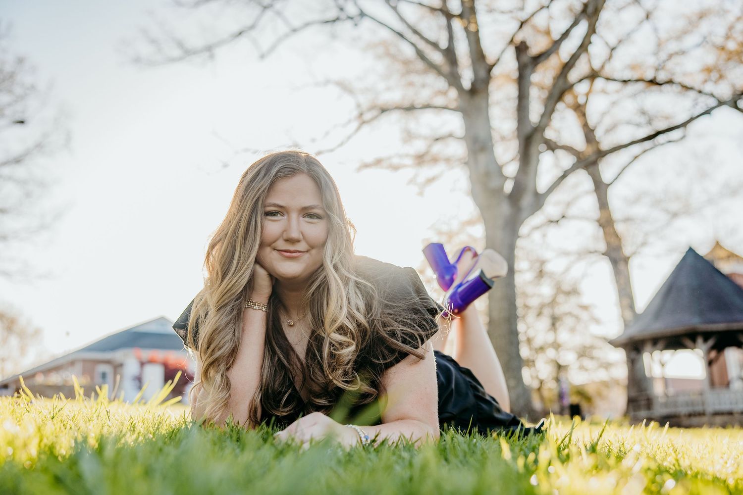 Graduate in black dress lying on grass during outdoor photo session.