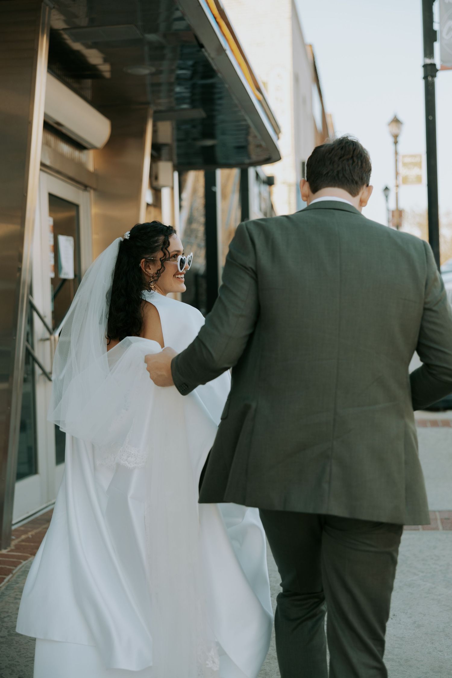 Wedding couple walking along sidewalk viewed from behind.
