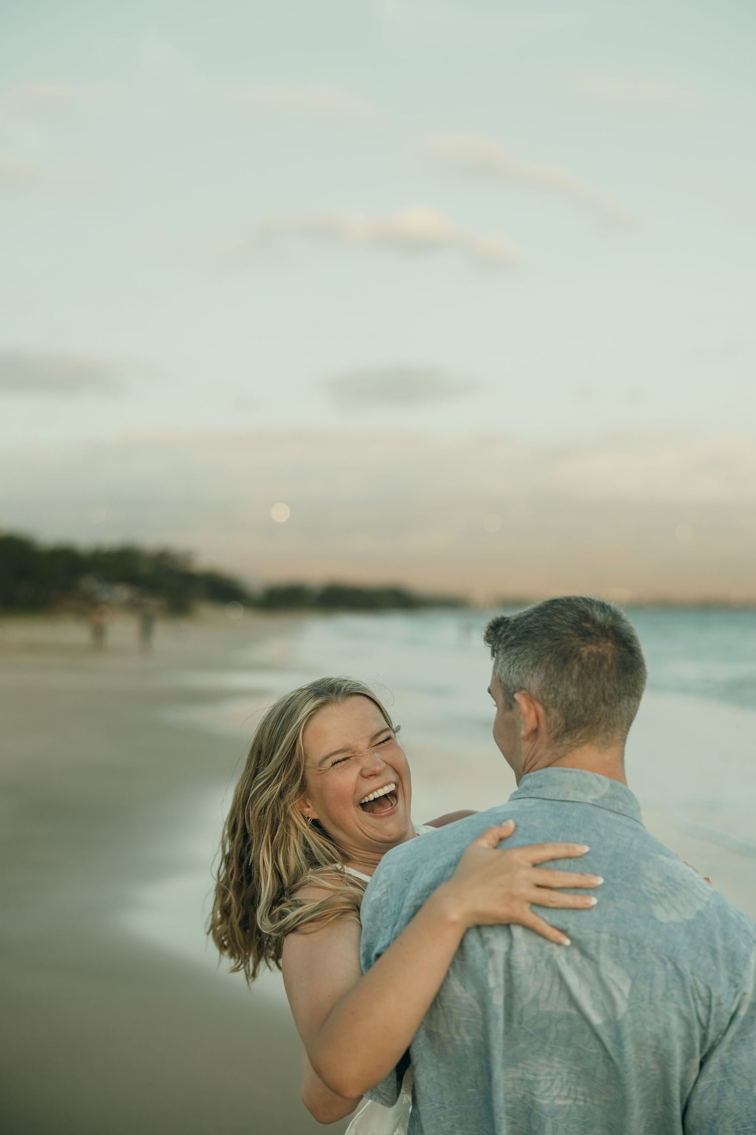 A romantic beach photoshoot sequence showing a couple laughing and embracing at sunset by the ocean.