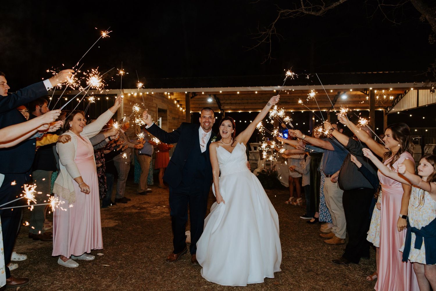 Newlyweds exit under sparkler send-off with guests lined up on both sides.