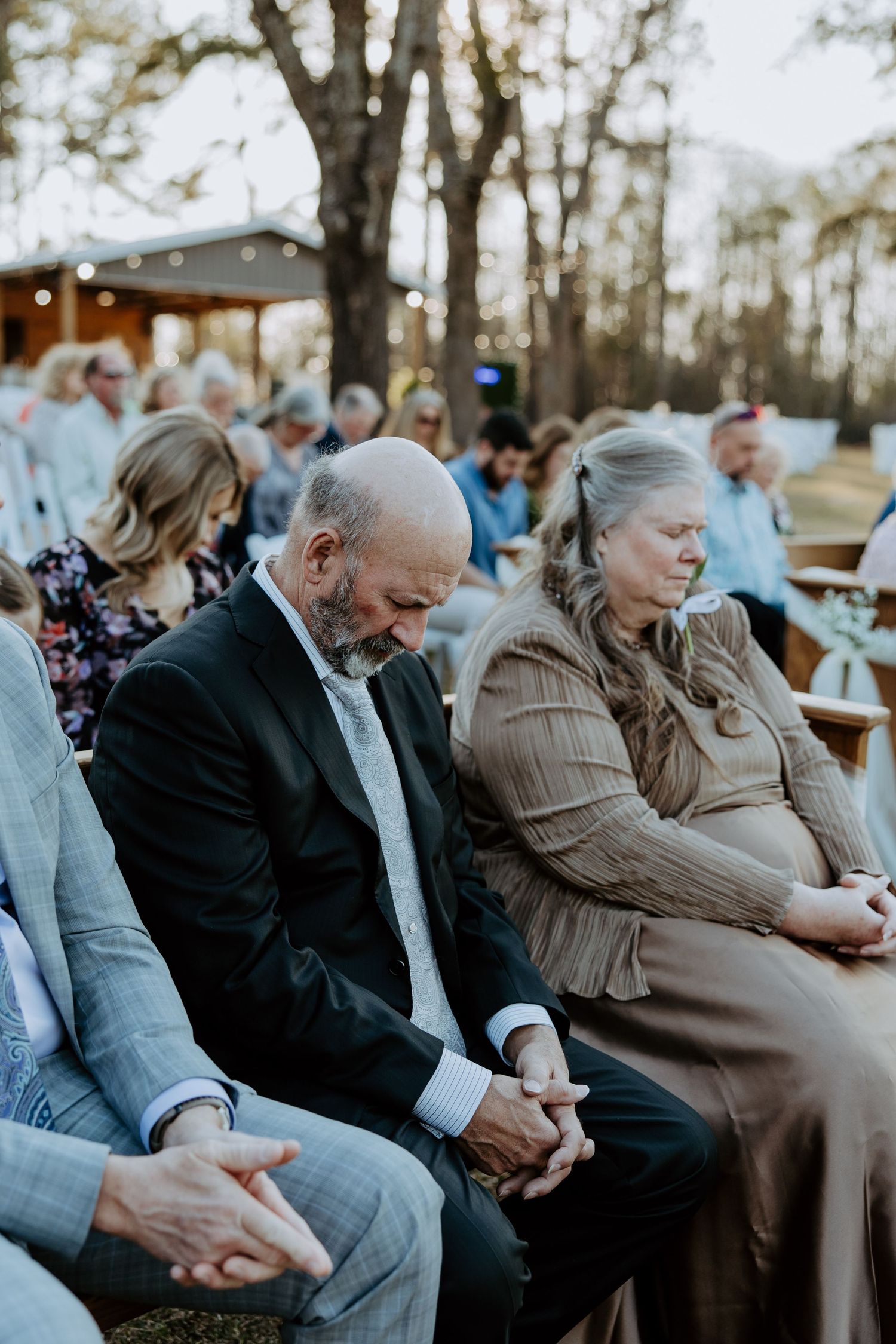 Wedding guests sitting during outdoor ceremony with mature couple in focus.