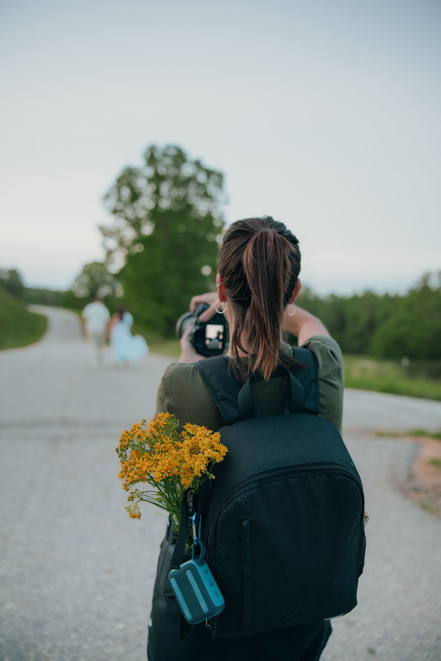 Back view of photographer with backpack and yellow flowers capturing nature on path.