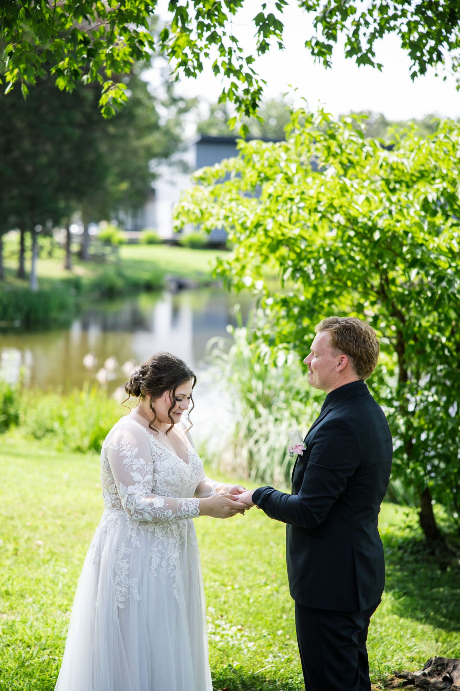 A couple shares an emotional first look moment in a garden setting with lush greenery and a pond in the background.