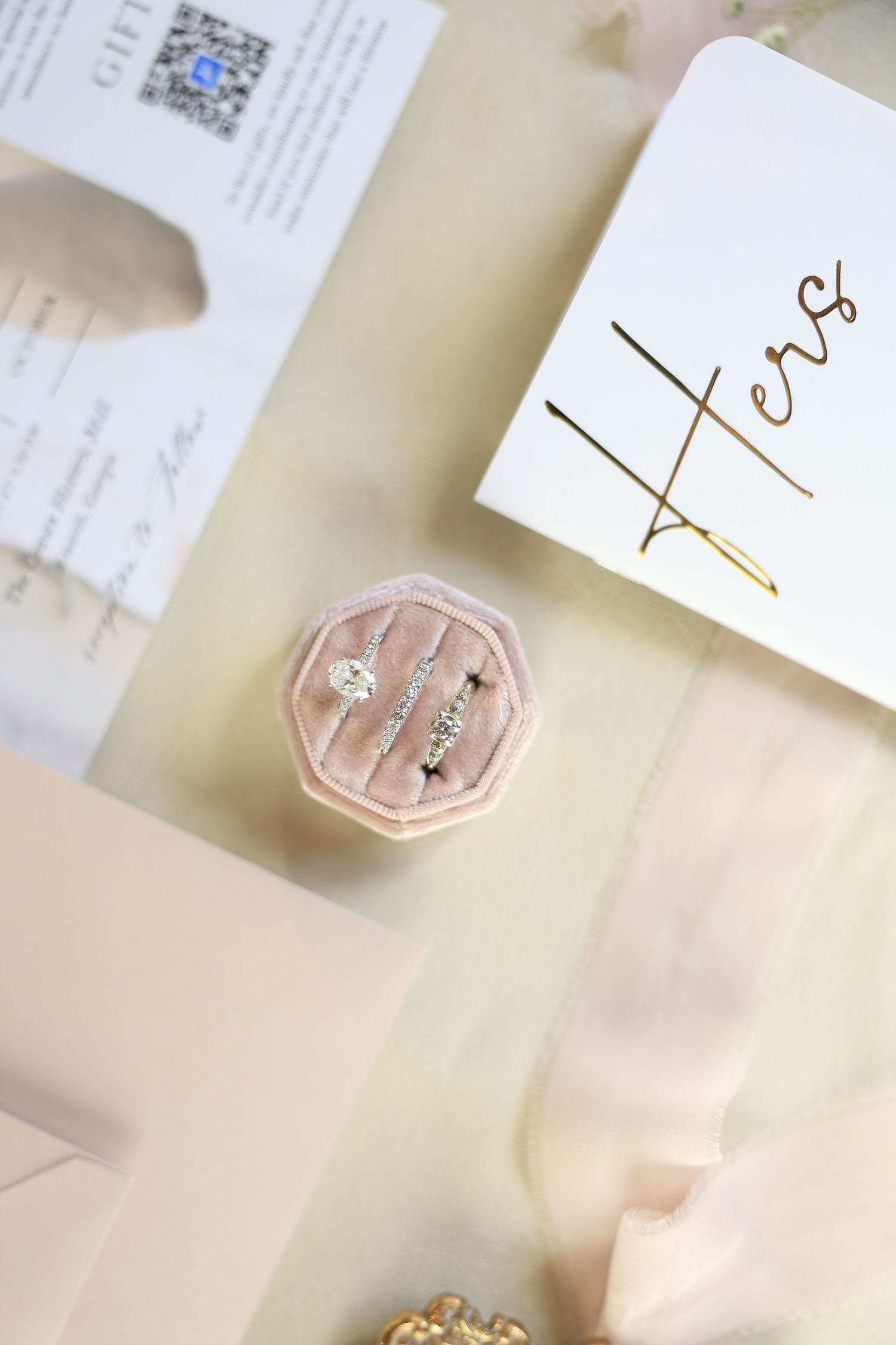 Two diamond rings displayed in a pink velvet octagonal ring box beside a Hers card and pink ribbon.