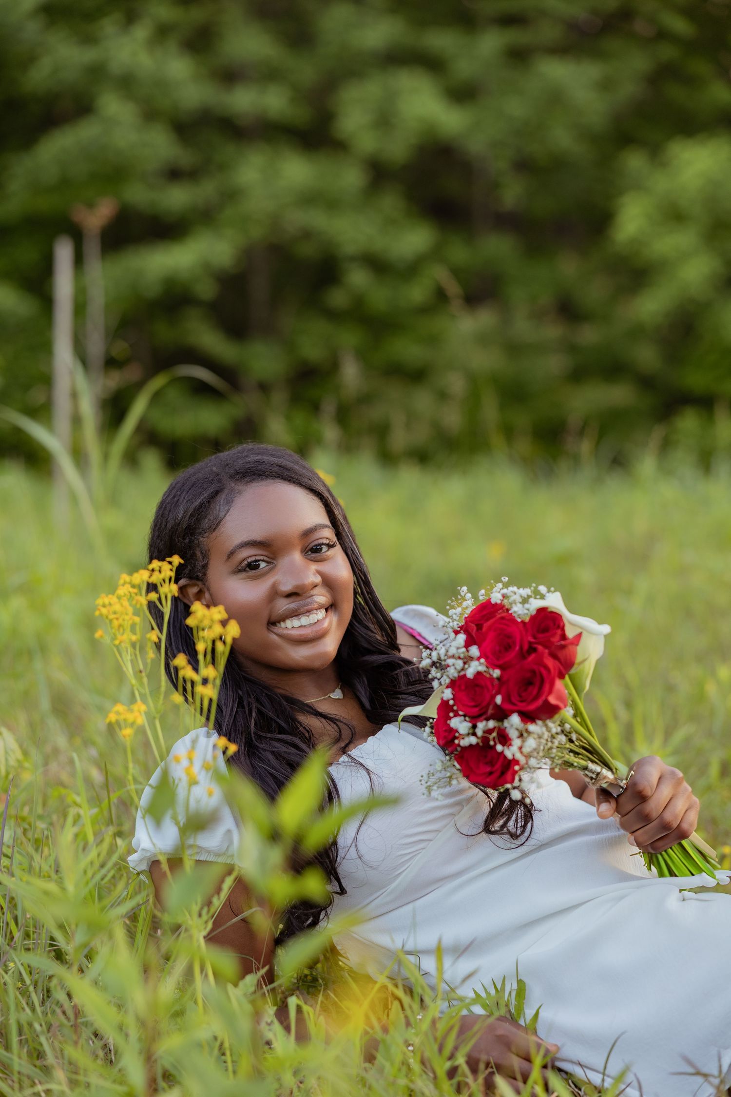 Someone lying in wildflowers holds a bouquet of red and yellow blooms.