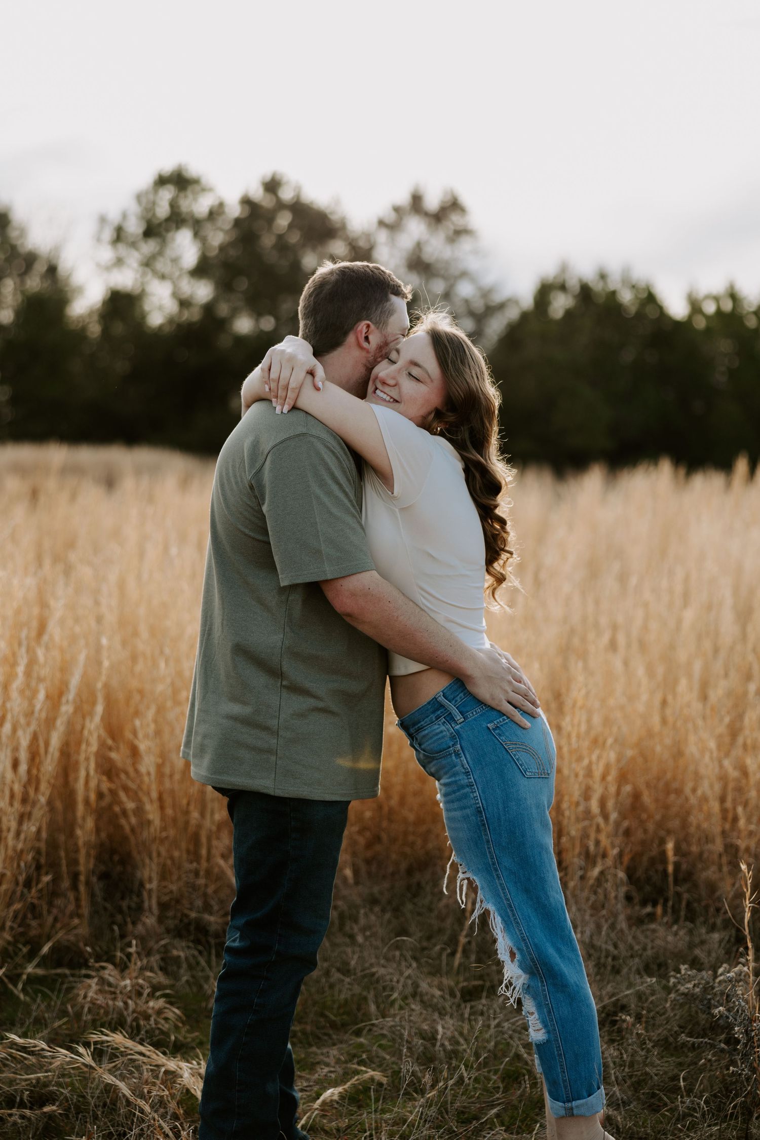A couple embraces in a golden field during sunset.