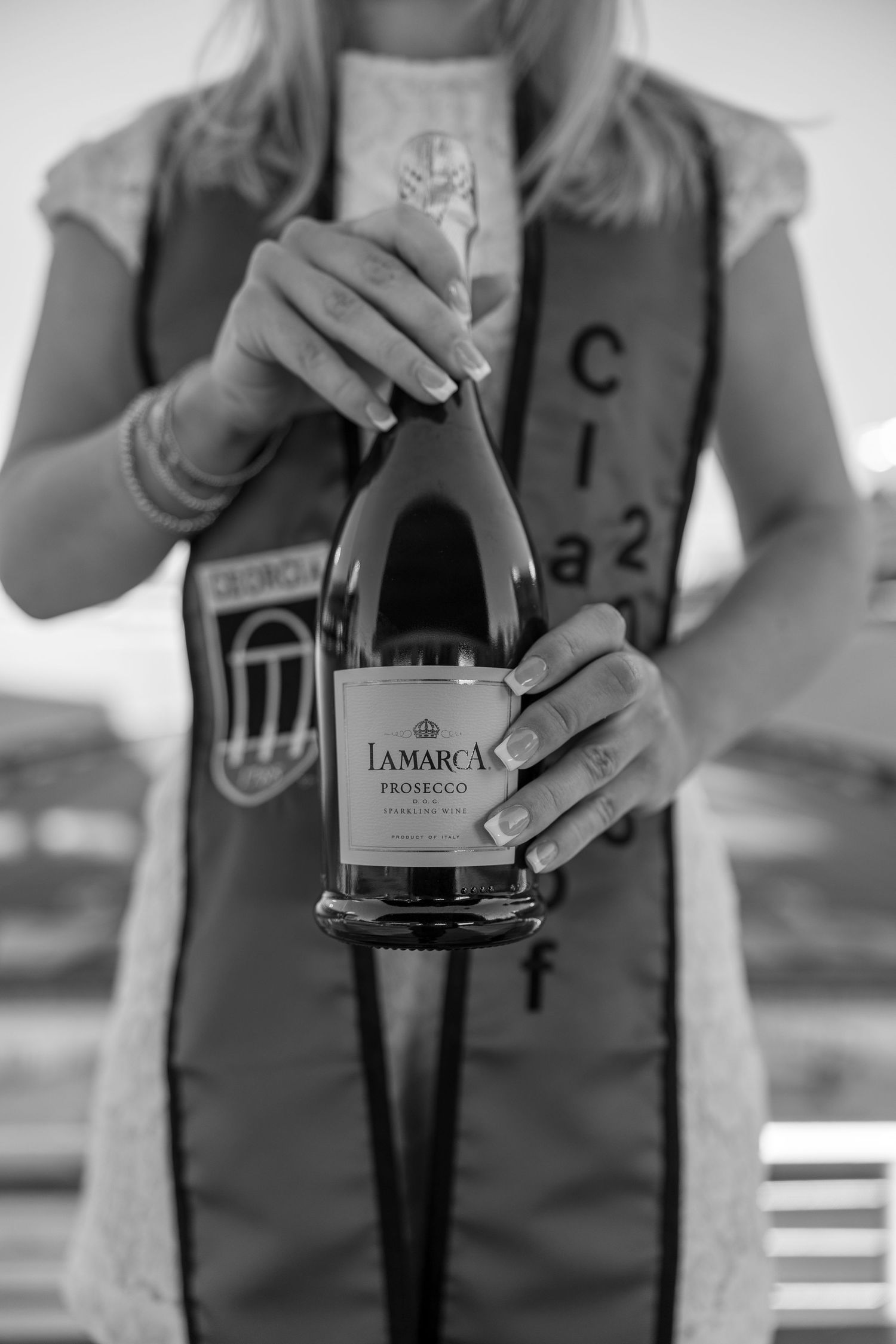 Close-up of hands holding La Marca Prosecco bottle with graduation stole visible.