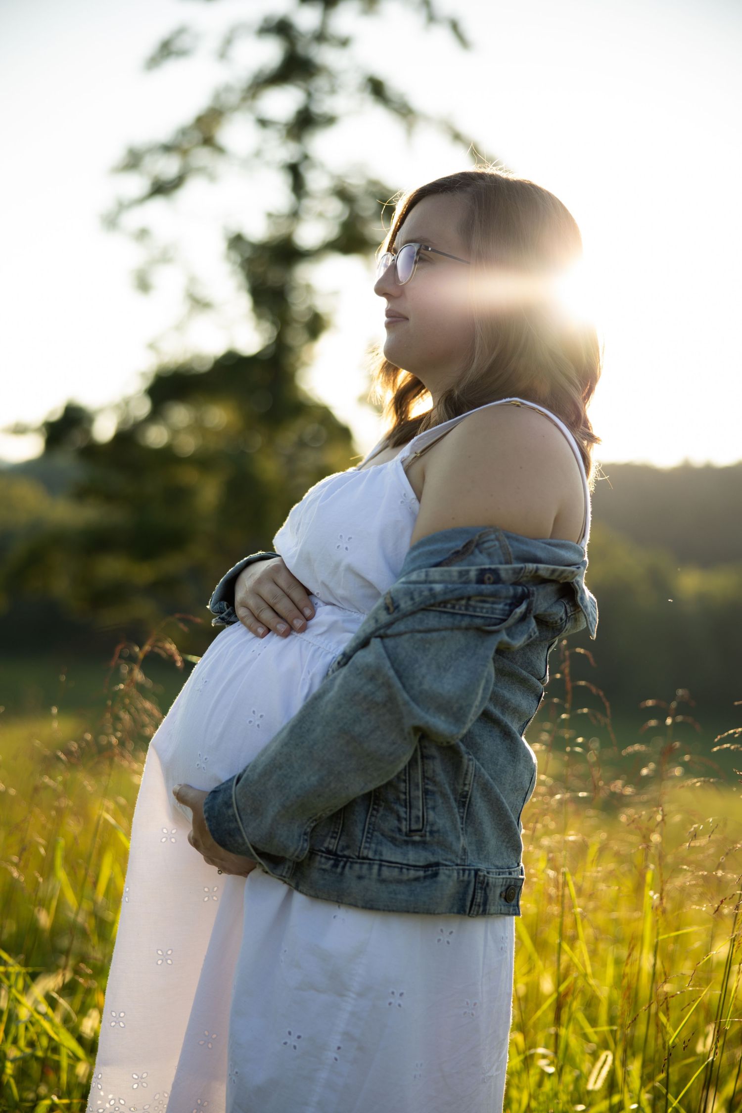 A couple embraces in a sunlit meadow at golden hour with tall grass and lens flare in the background.